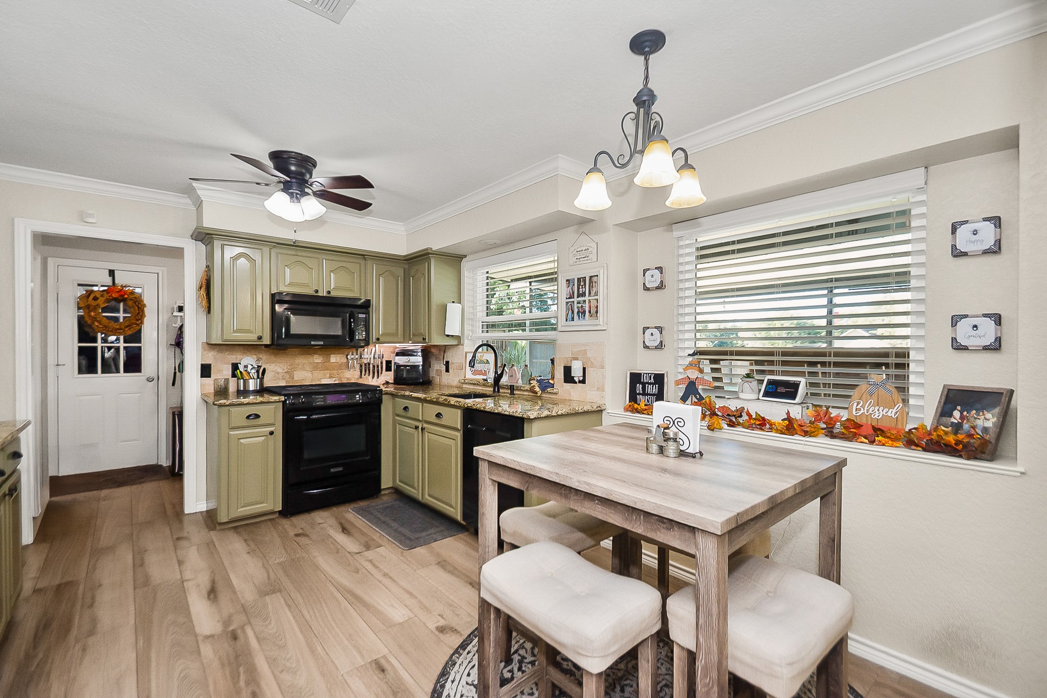Charming kitchen with olive green cabinets, modern black appliances, and a cozy breakfast nook by a large window, offering ample natural light and a welcoming atmosphere.