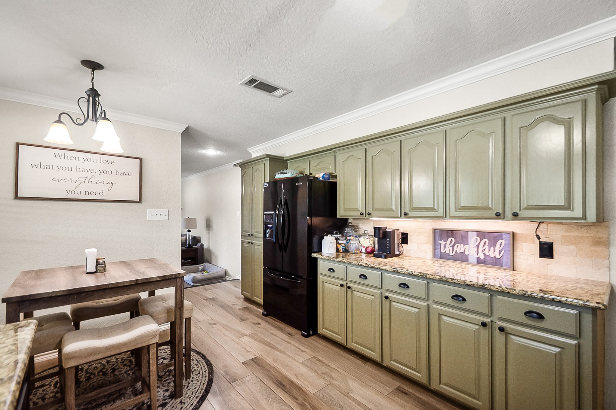 Charming kitchen with sage green cabinetry, granite countertops, and a cozy dining area under warm pendant lighting, perfect for intimate meals.