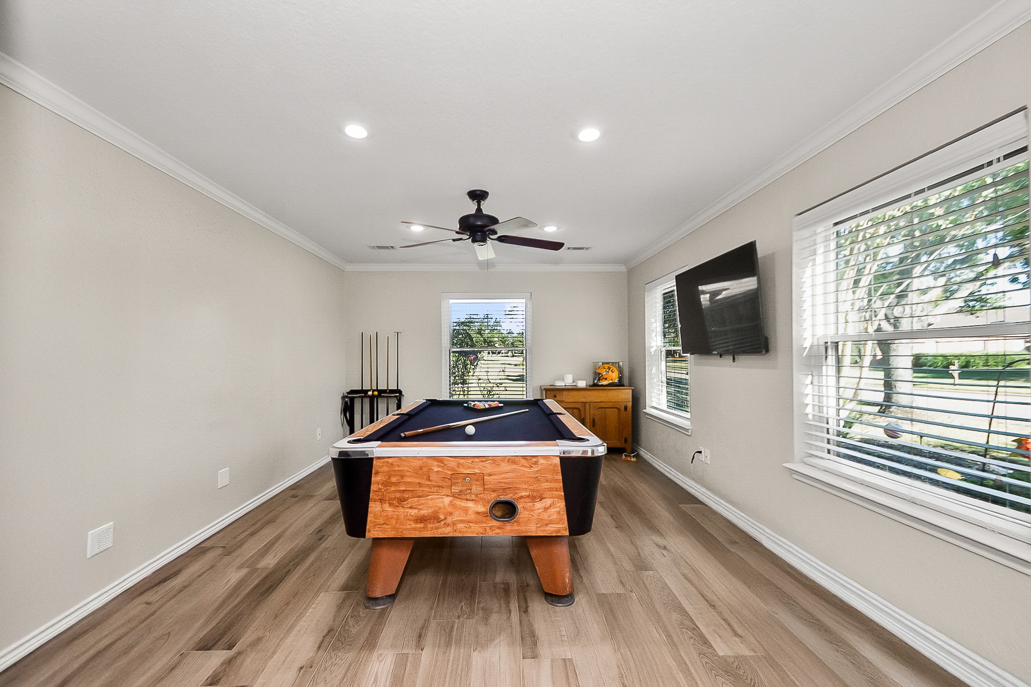 Spacious game room featuring a stylish pool table, sleek wood look flooring, and abundant natural light from large windows, perfect for entertaining and relaxation.