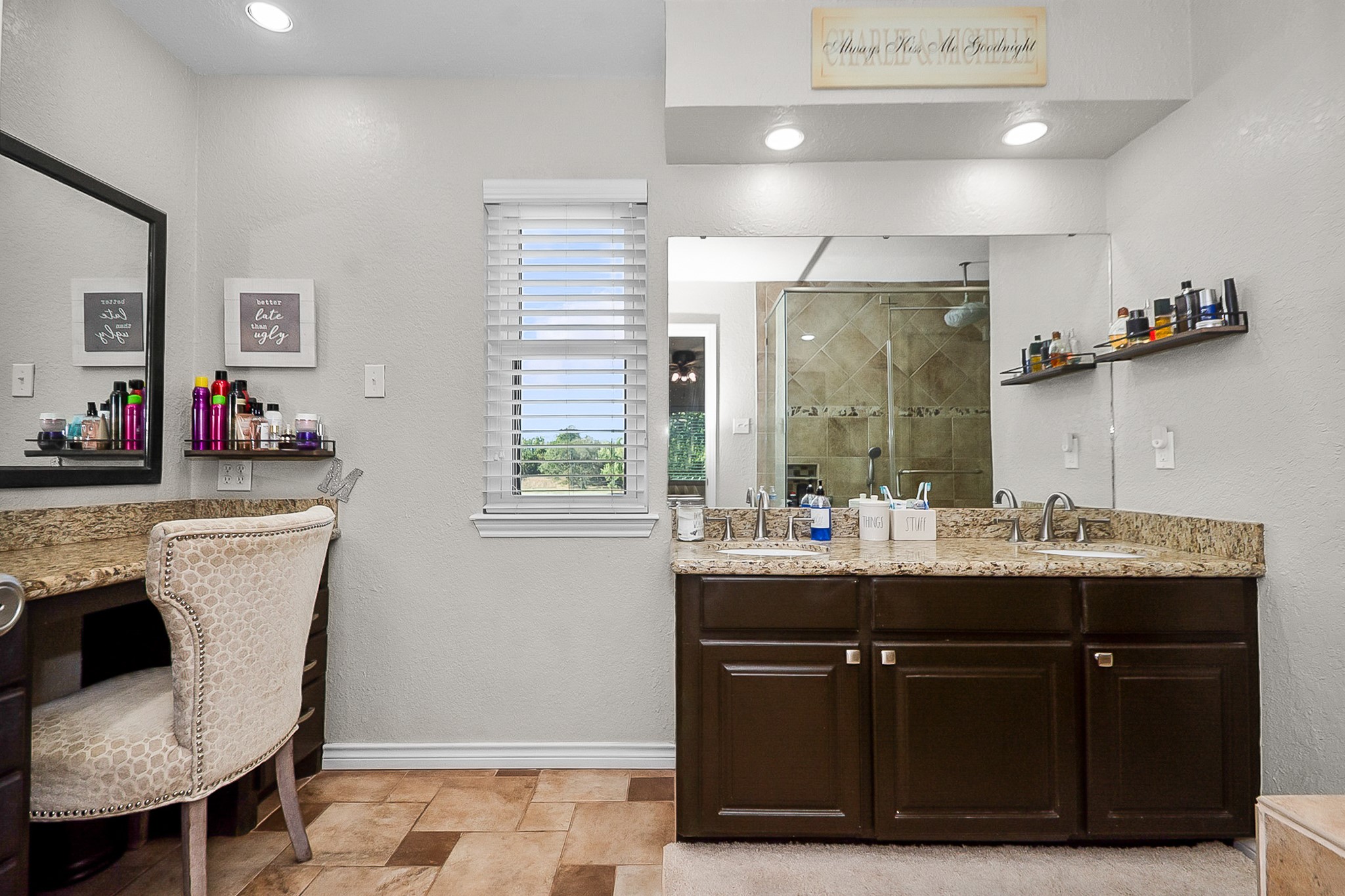 Elegant bathroom featuring dual sinks with granite countertops, a spacious vanity area, and a large mirror. Natural light flows through the window, highlighting the stylish tile flooring and modern fixtures.
