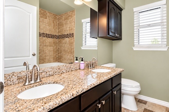 Elegant bathroom featuring a dual-sink granite countertop, rich dark cabinetry, and a tiled shower area with a decorative accent strip.