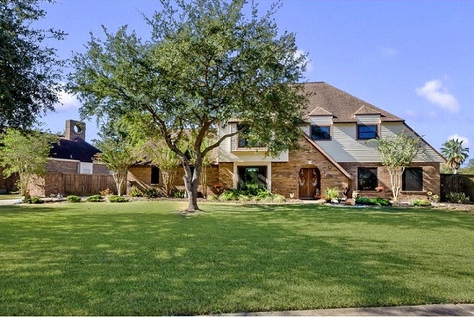 Charming two-story home with a classic brick facade, nestled on a spacious, manicured lawn with mature trees offering shade and privacy.