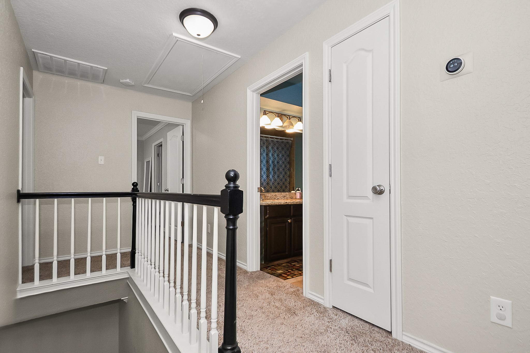 Bright and inviting upstairs landing with plush carpeting and elegant railing, leading to a well-appointed bathroom featuring a granite countertop.