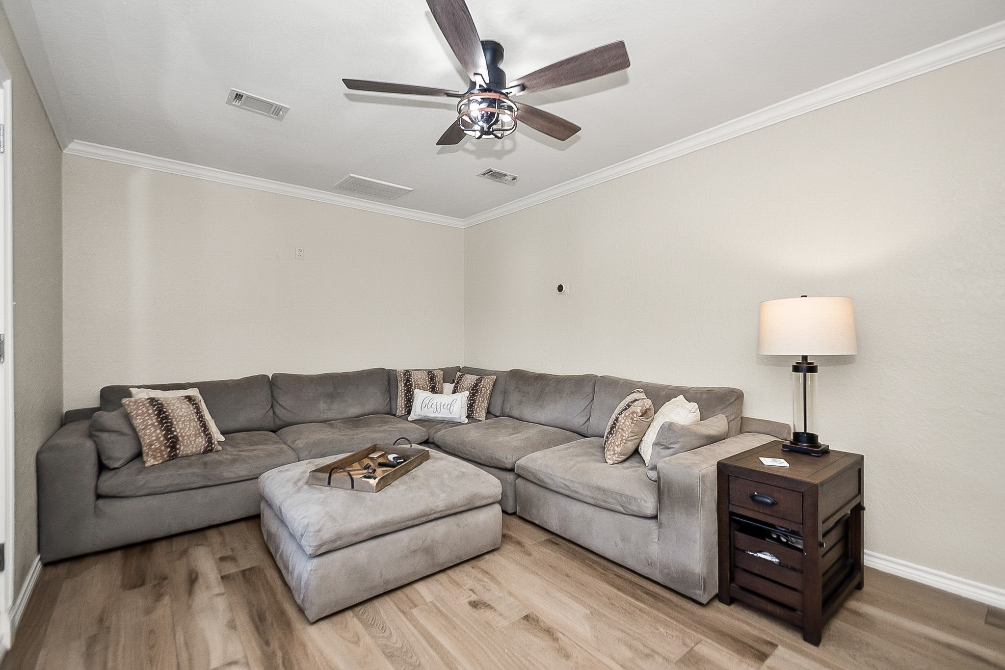 Cozy living area featuring a spacious L-shaped sectional sofa, warm wood like flooring, and a ceiling fan for comfort and style.