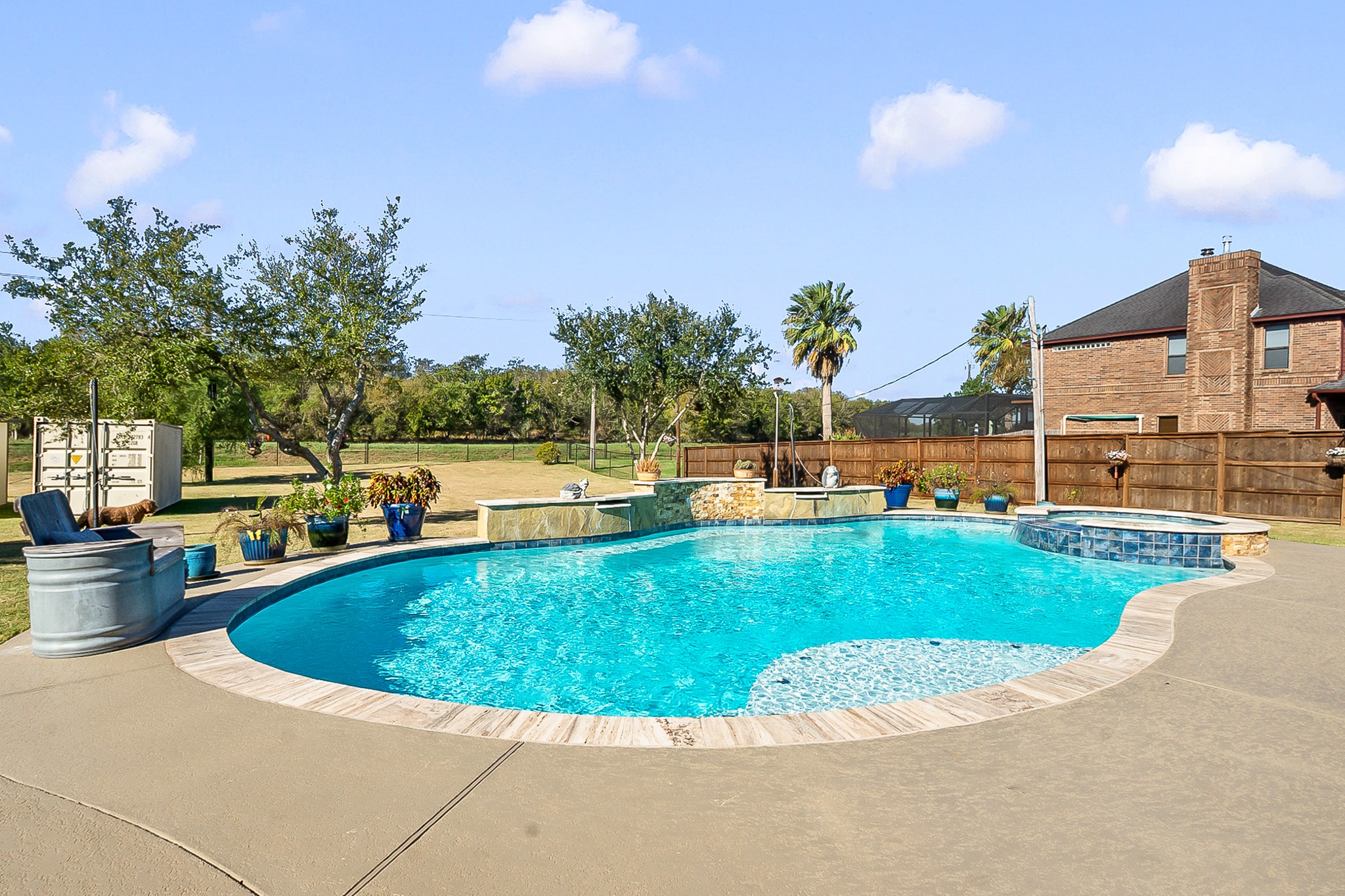 Experience outdoor luxury with a sparkling heated pool surrounded by lush landscaping, ample patio space, and a charming stone accent wall. Perfect for relaxation and entertaining.