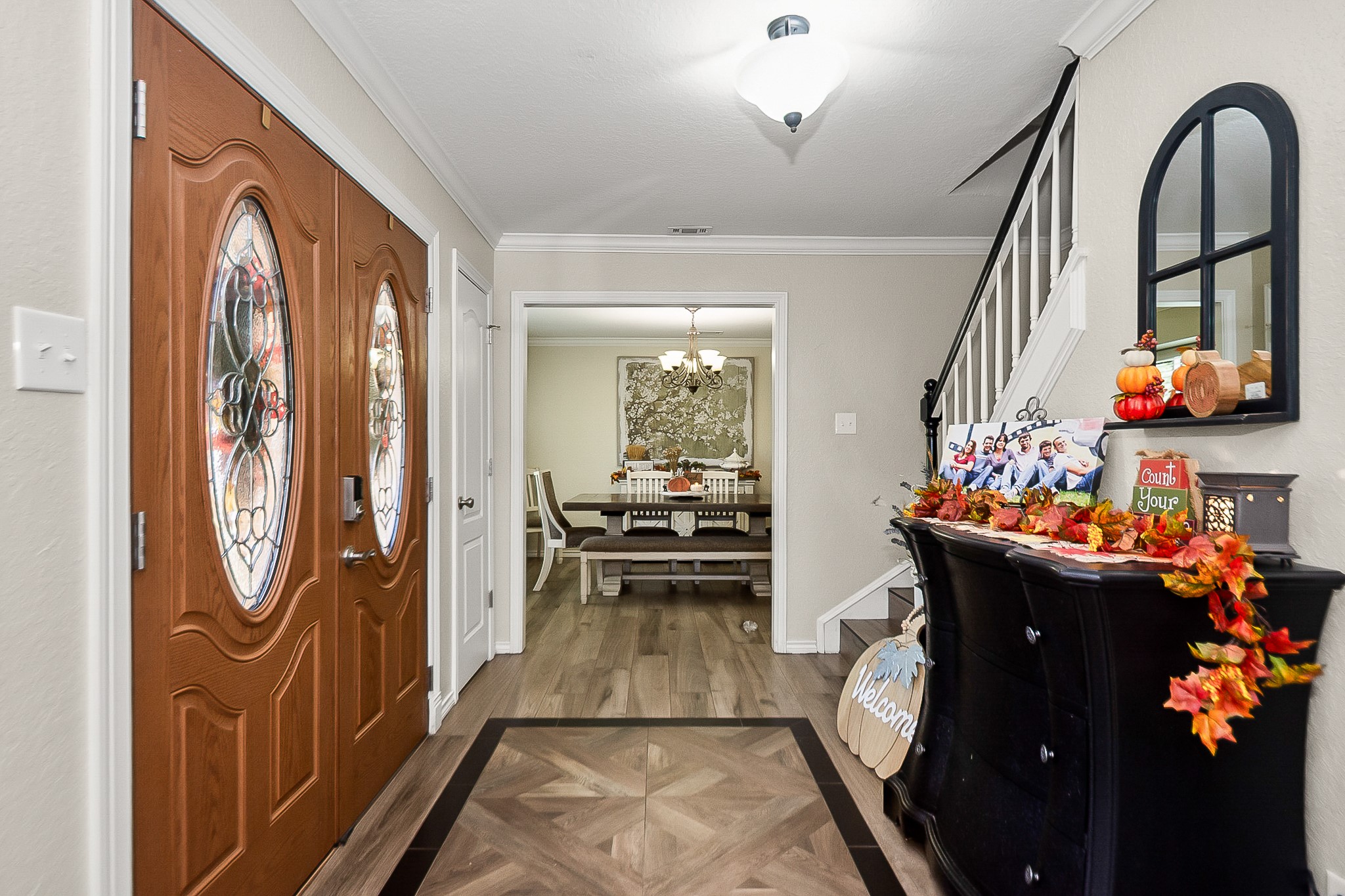 Elegant entryway featuring double doors with decorative glass, leading to a cozy dining area. The space is accentuated by warm wood look flooring.