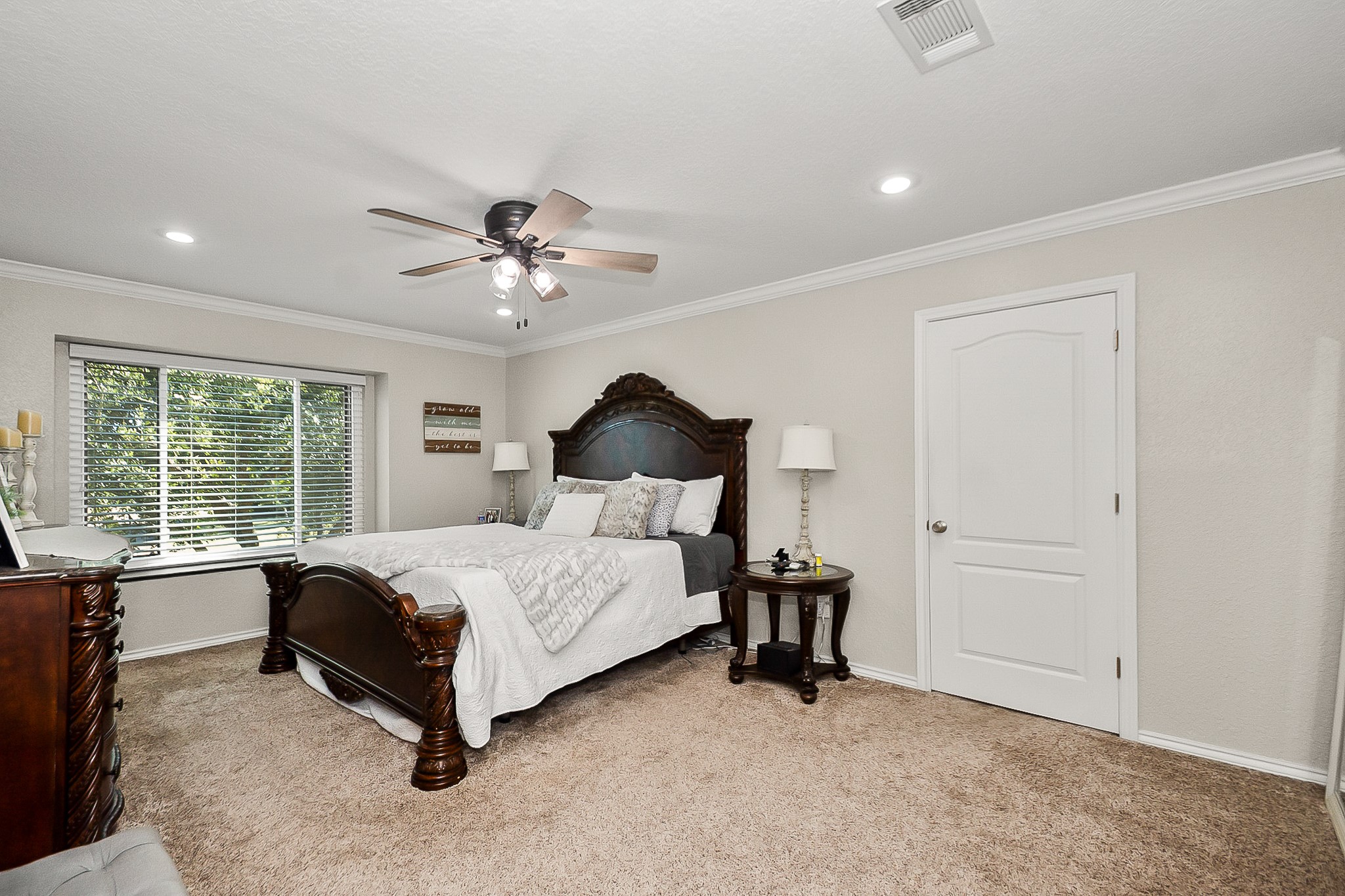Spacious Primary bedroom featuring plush carpeting, a ceiling fan, and a large window inviting natural light, complemented by elegant wooden furniture for a cozy retreat.
