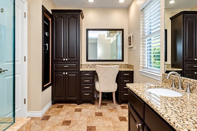 Elegant bathroom featuring rich dark wood cabinetry, granite countertops, and a cozy vanity area, complemented by warm tile flooring and abundant natural light.