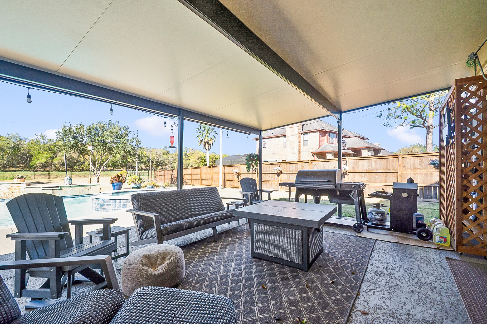 Enjoy outdoor living in this spacious 988 sq. ft. covered patio featuring comfortable seating, a grill for barbecues, and a view of the inviting pool, perfect for relaxation and entertaining.