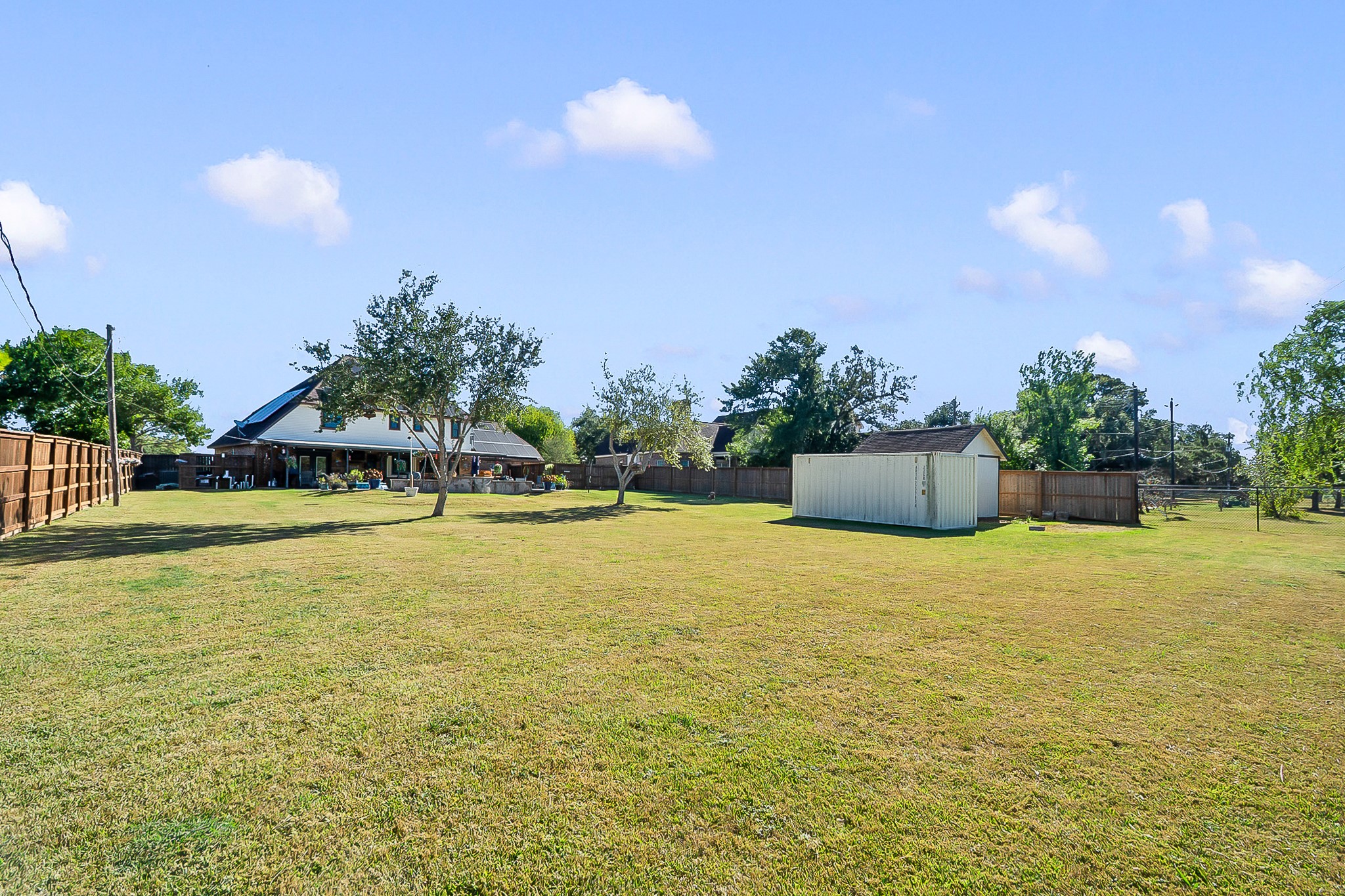 Expansive backyard with lush green lawn, mature trees, and a storage shed, perfect for outdoor activities.