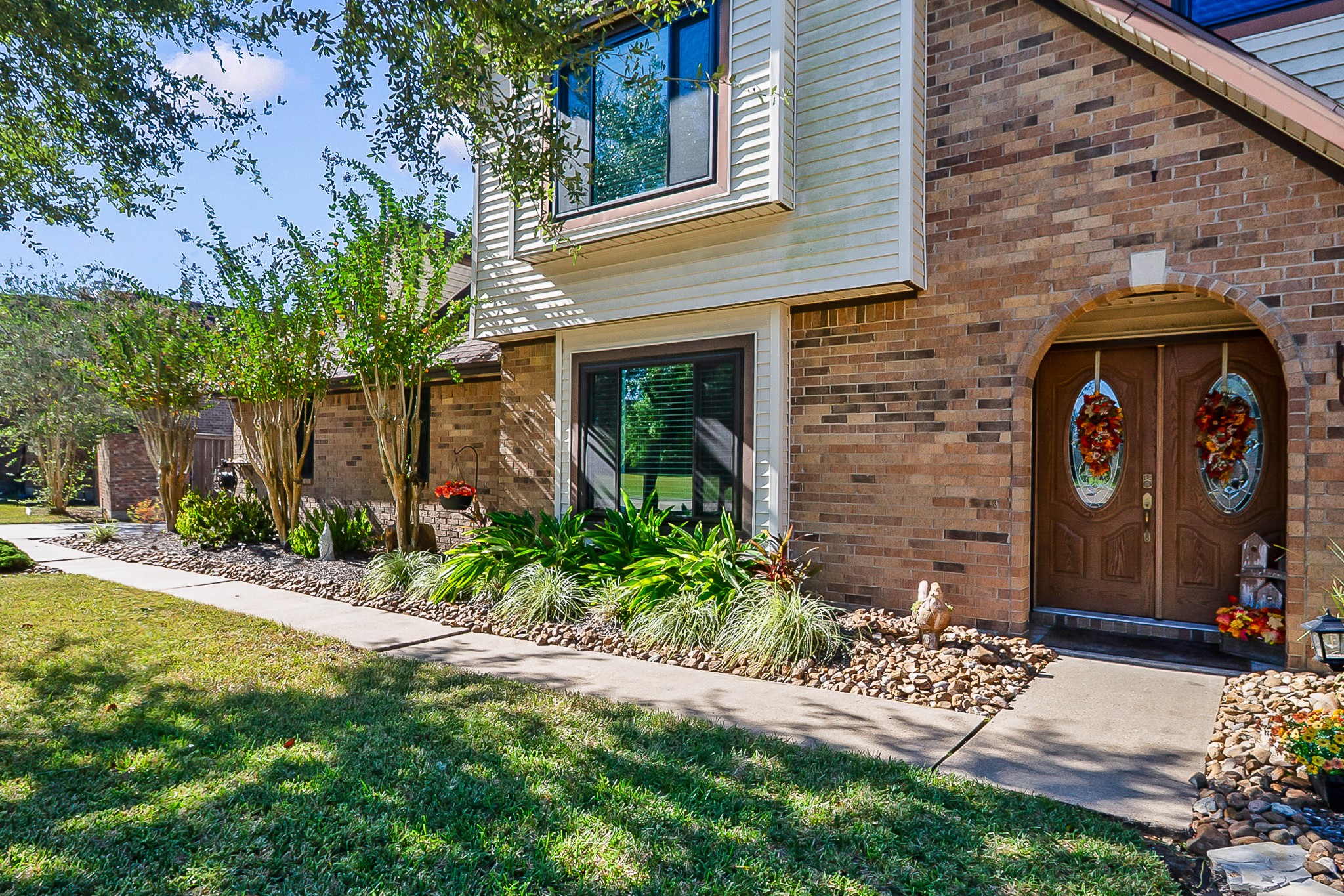 Charming brick home with elegant arch-top double doors, lush landscaping, and a welcoming walkway.