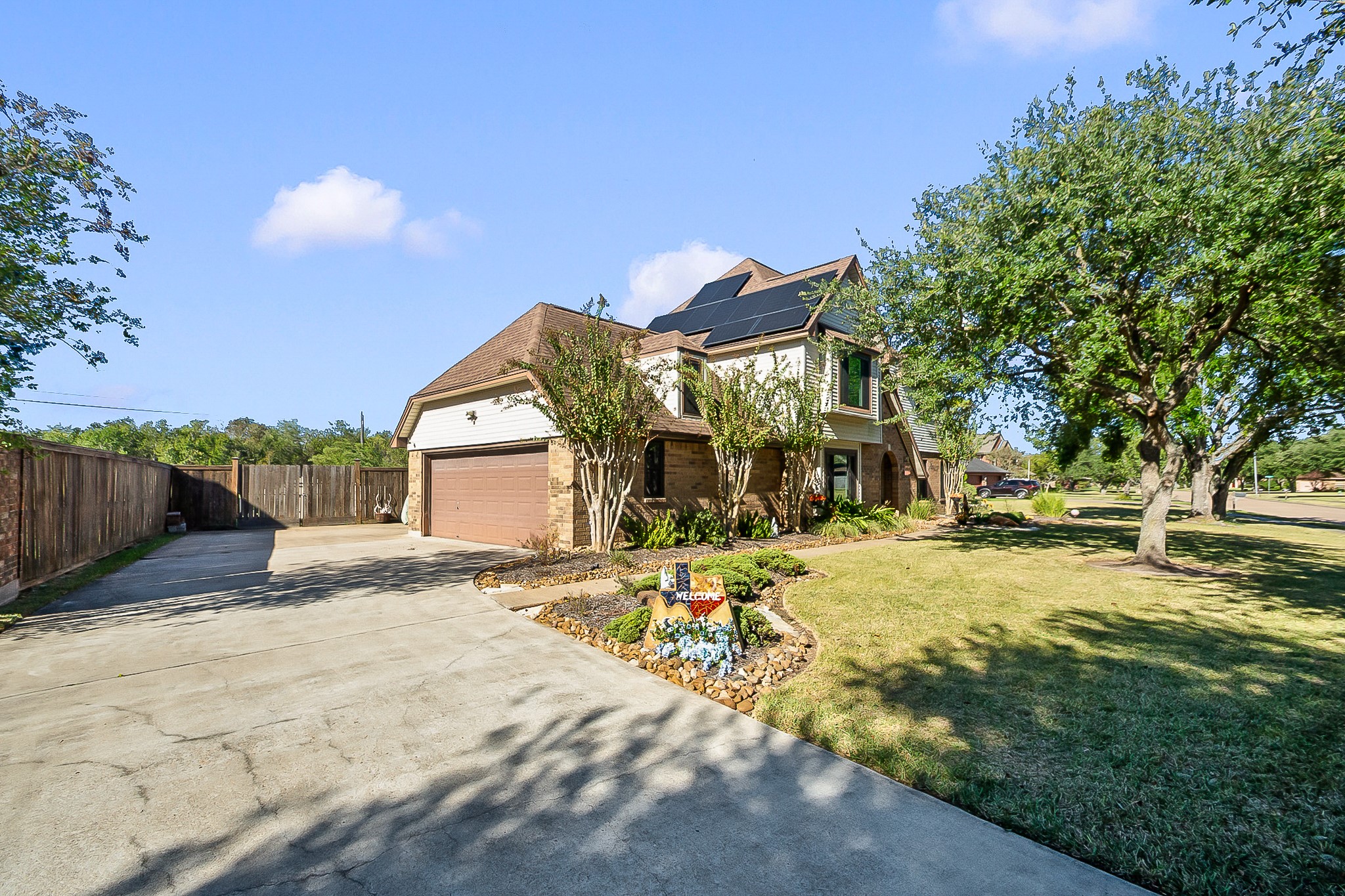 Spacious two-story home with paid off solar panels, featuring a large driveway, attached garage, and beautifully landscaped yard with mature trees.