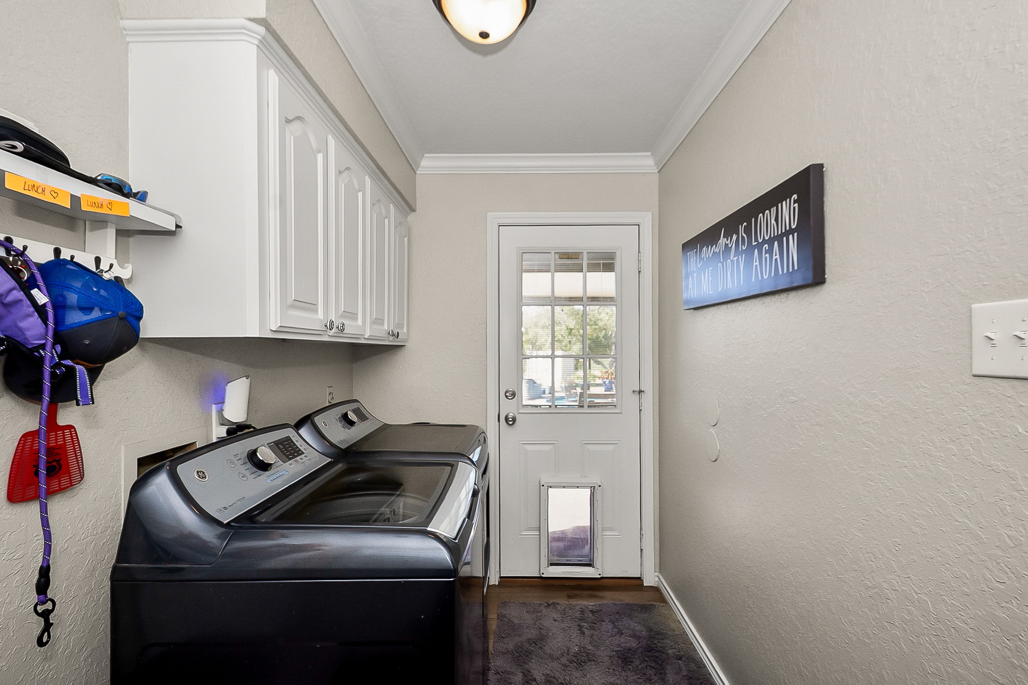 Bright and functional laundry room featuring modern appliances, ample storage with overhead cabinets, and a convenient exterior door with glass paneling.