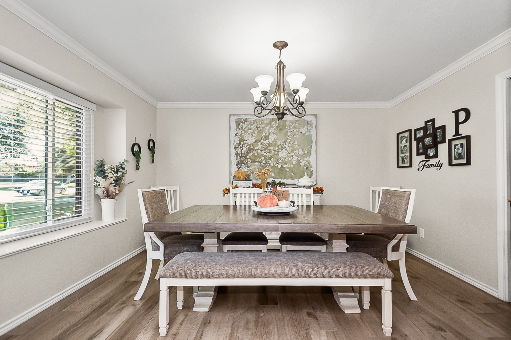 Charming dining room with elegant wood like flooring, a large window offering abundant natural light, and a stylish chandelier above a spacious table with ample seating for gatherings.