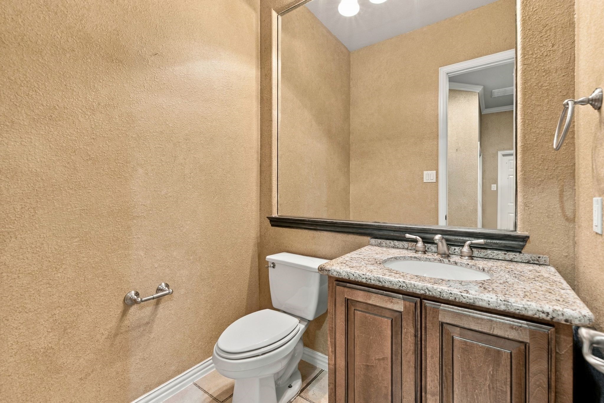 Charming powder room features a granite countertop, elegant fixtures, and a large mirror, creating a welcoming and functional space.