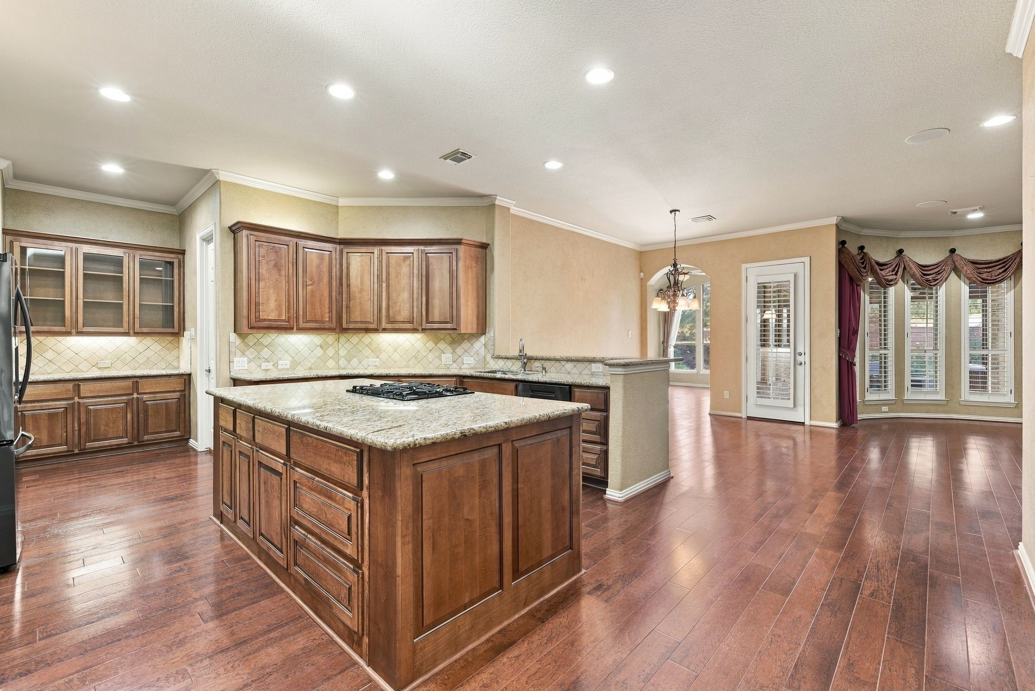 Spacious kitchen with rich wooden cabinetry, granite countertops, and a central island with a gas cooktop. The open layout flows into the breakfast area. Spacious kitchen with rich wooden cabinetry, granite countertops, and a central island with a gas cooktop. The open layout flows into the breakfast area.