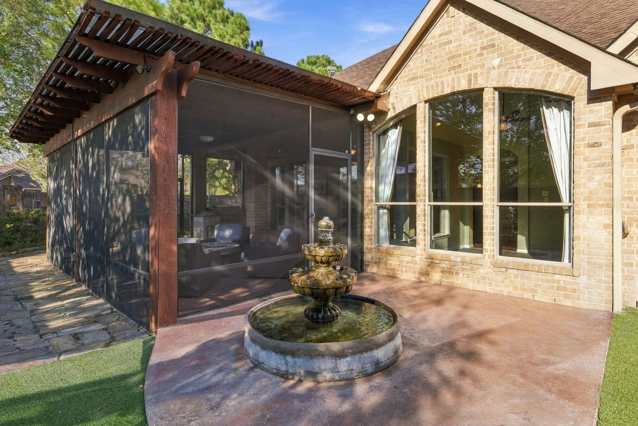 Charming brick exterior with large arched windows and a delightful screened-in patio, complemented by a serene, tiered fountain on a spacious stone patio.