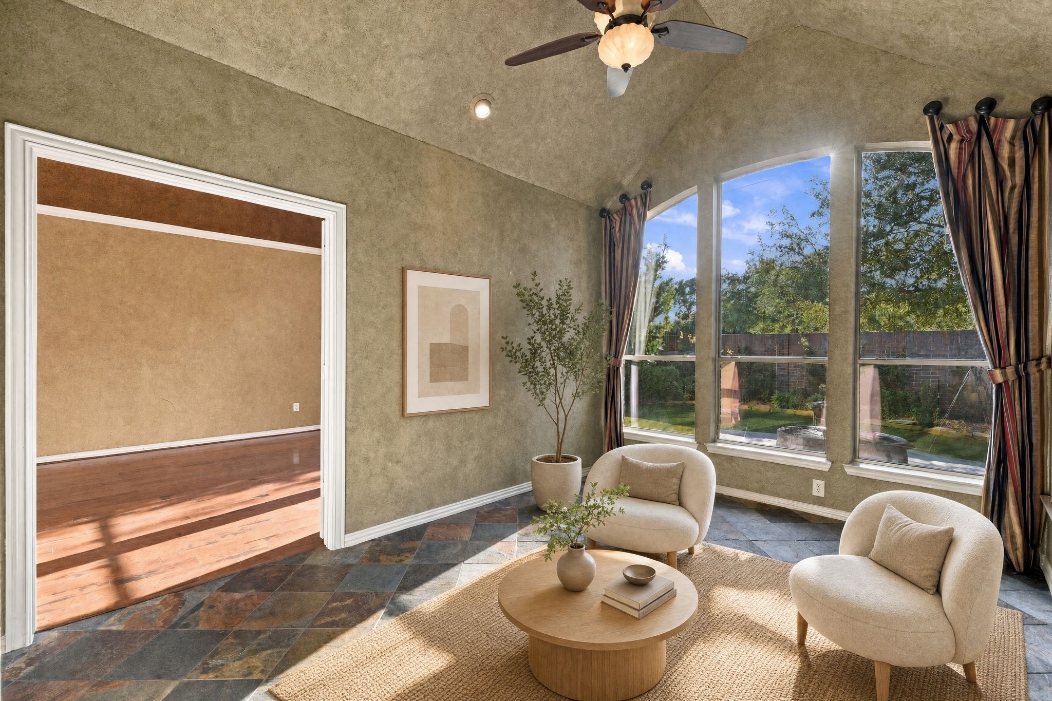 Inviting sunroom with vaulted ceilings, large arched windows offering abundant natural light, and a seamless flow into the adjoining primary bedroom. Space is virtually staged.