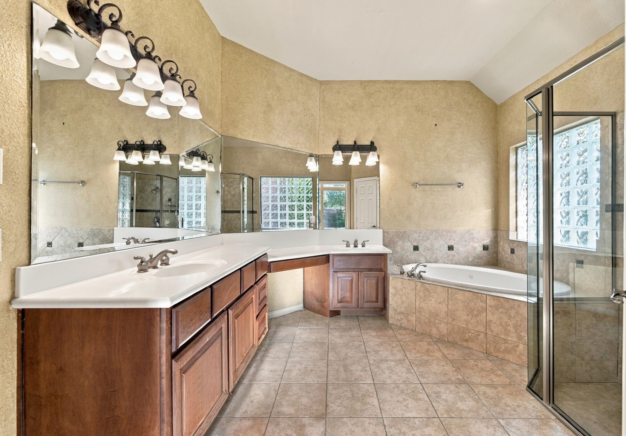 Spacious bathroom featuring a dual-sink vanity, elegant lighting, a luxurious soaking tub, and a glass-enclosed shower.