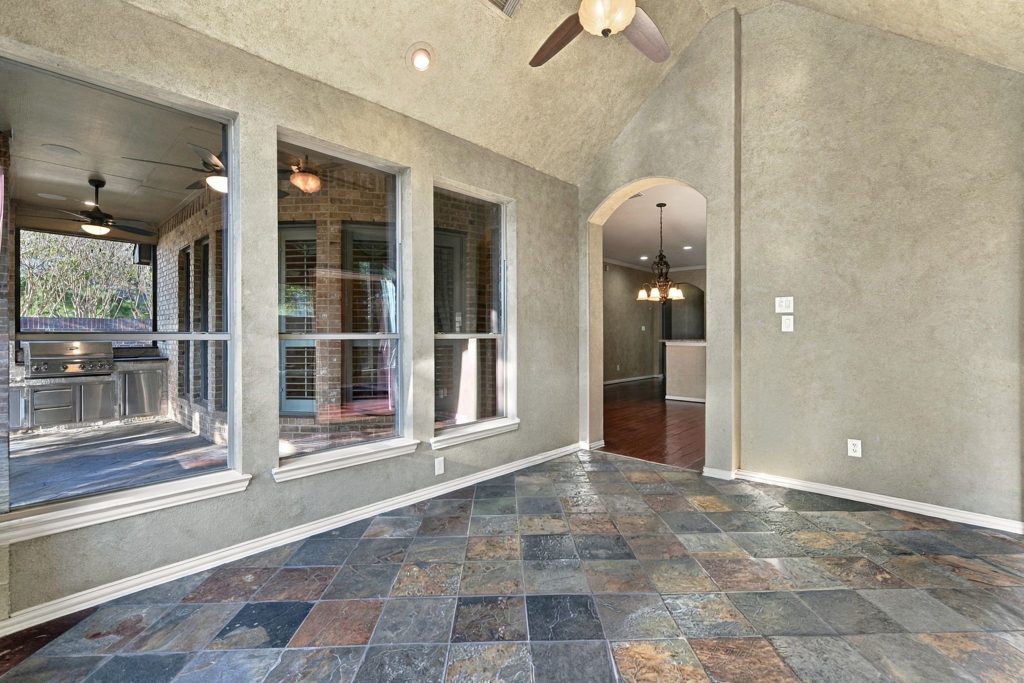 Bright sunroom with elegant slate flooring and large windows overlooking a covered patio. Perfect for entertaining and seamless indoor-outdoor living.
