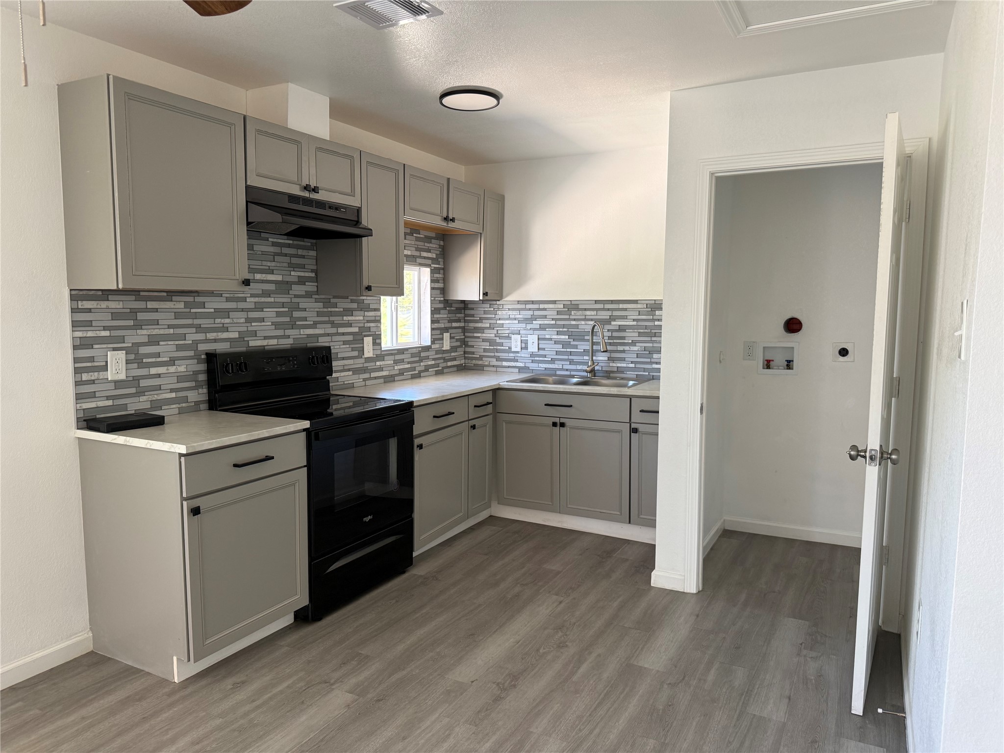 Updated kitchen with gray shaker cabinets, mosaic tile backsplash and an electric range.