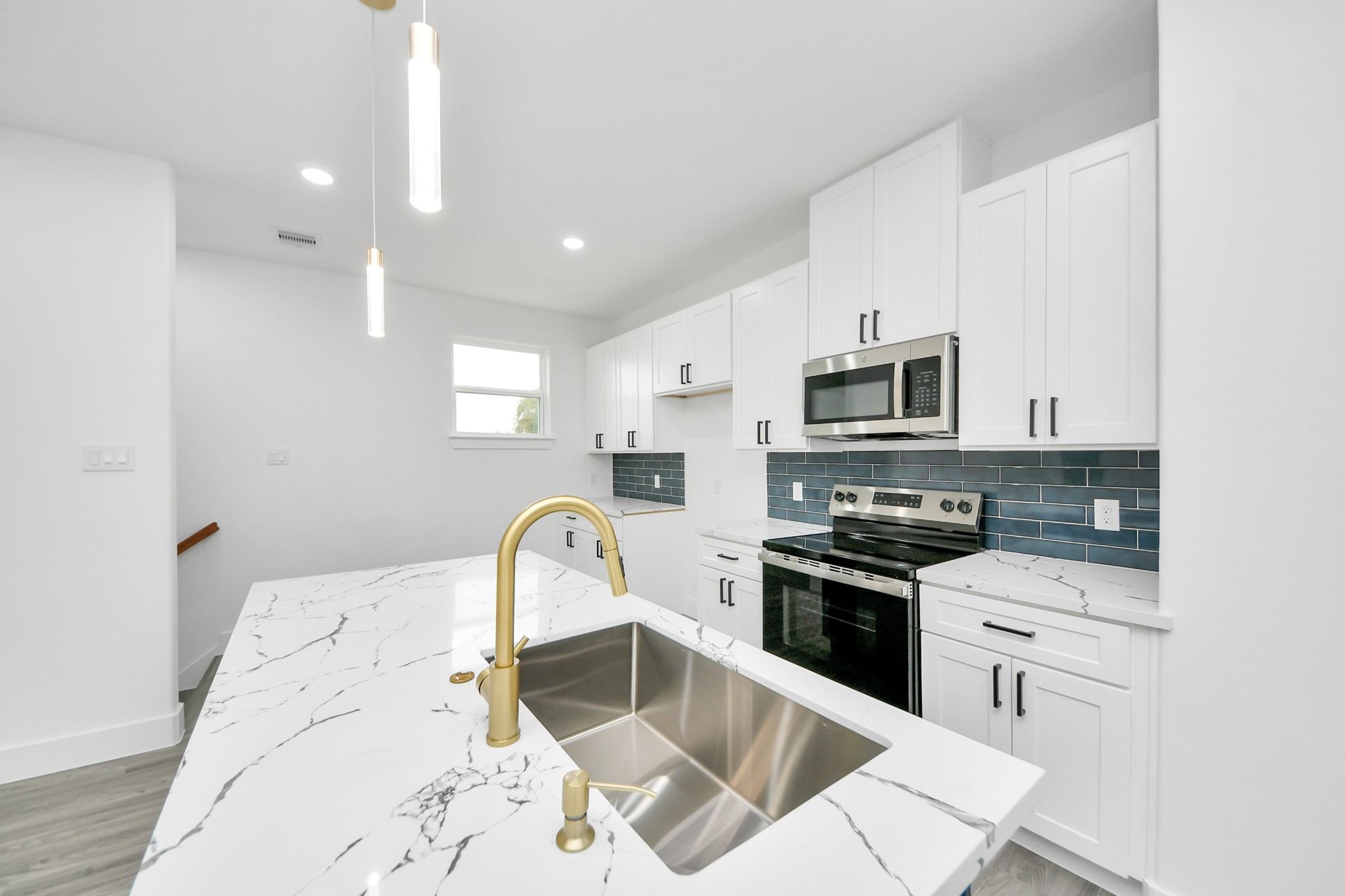 Sleek modern kitchen featuring elegant white cabinetry, a striking marble countertop island with a gold faucet, and stainless steel appliances complemented by a stylish dark blue backsplash.
