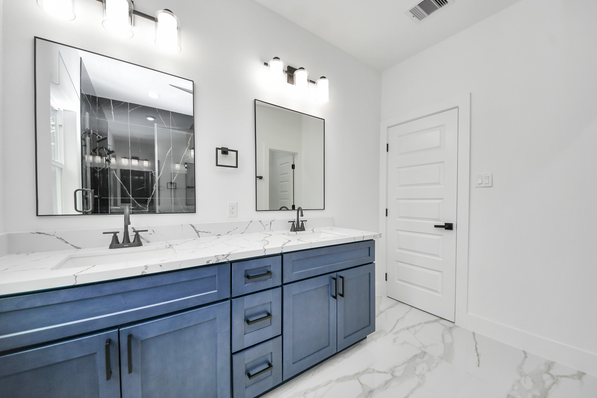 Elegant bathroom featuring a double vanity with striking blue cabinetry, marble countertops, and modern fixtures, complemented by sleek mirrors and contemporary lighting.