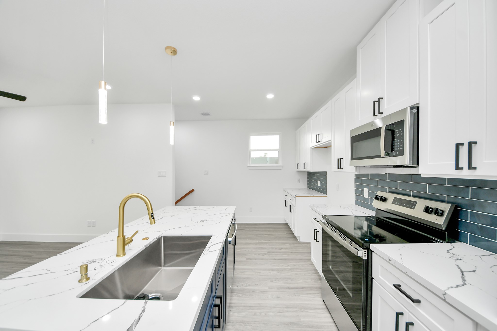 Sleek modern kitchen with elegant white cabinetry, marble countertops, and a stylish gold faucet. Features include stainless steel appliances, a dark blue tile backsplash, and ample lighting for a bright, inviting space.