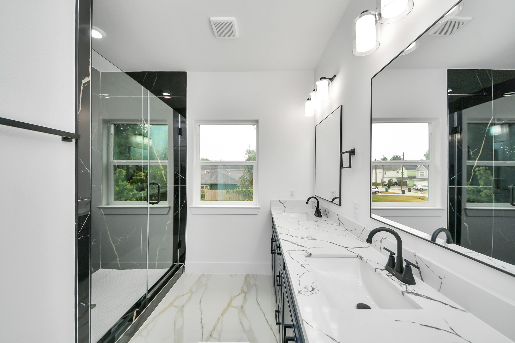 Elegant bathroom featuring a spacious dual-sink vanity with sleek black fixtures and luxurious marble countertops, complemented by a modern glass-enclosed shower. Elegant bathroom featuring a spacious dual-sink vanity with sleek black fixtures and luxurious marble countertops, complemented by a modern glass-enclosed shower.