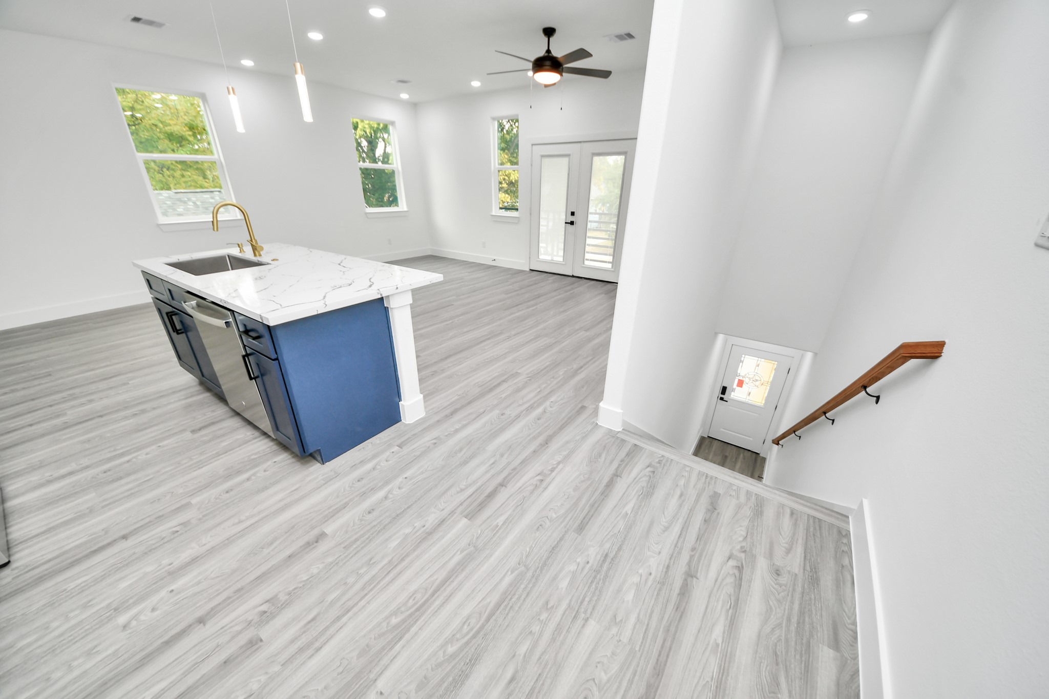 Bright and spacious open-concept living area featuring modern gray flooring, a sleek kitchen island with a marble countertop, and large windows for natural light.