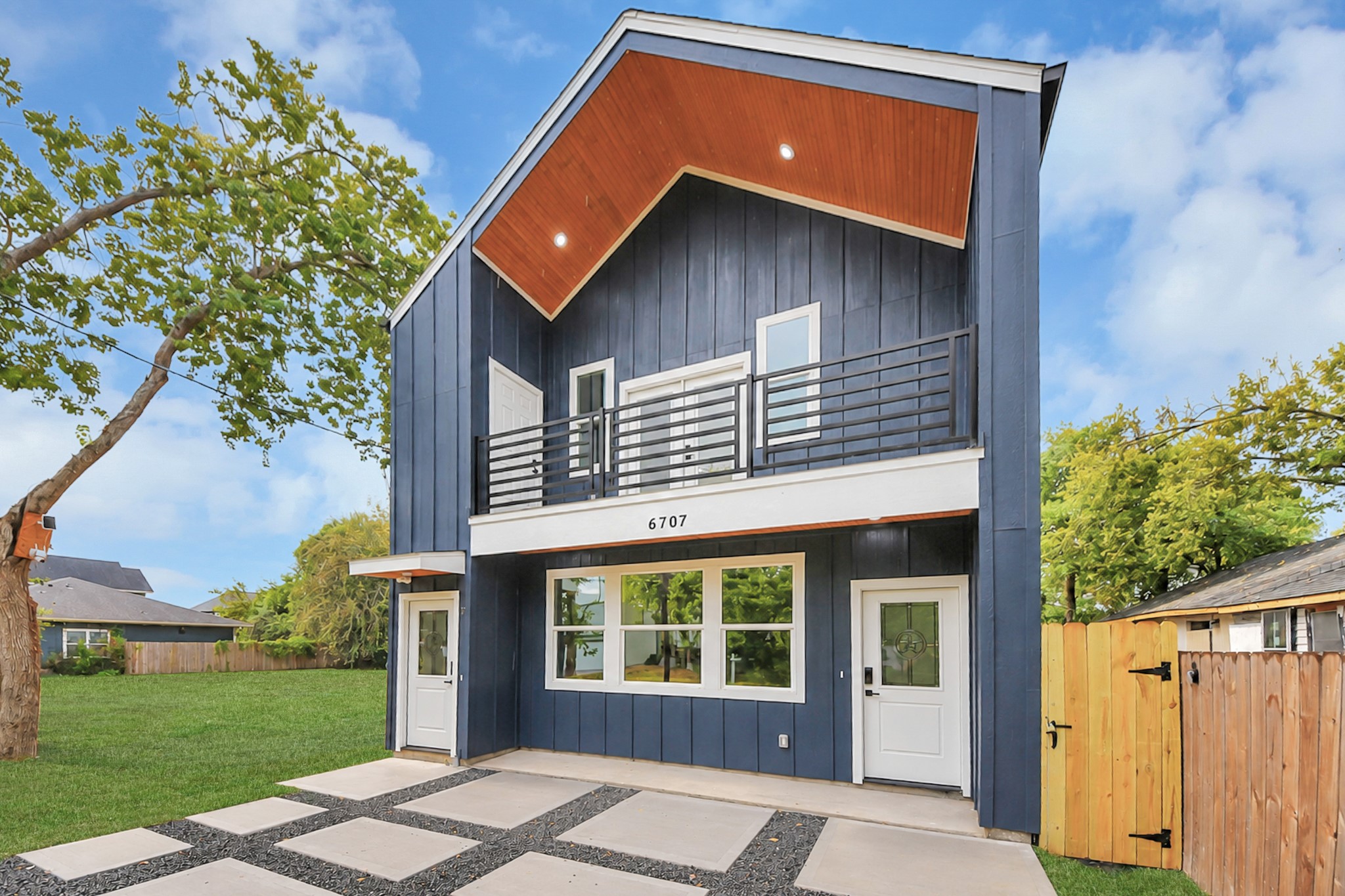 Modern two-story home with a striking navy faade, featuring a sleek balcony and a welcoming front entrance, set against a backdrop of lush greenery. Modern two-story home with a striking navy faade, featuring a sleek balcony and a welcoming front entrance, set against a backdrop of lush greenery.