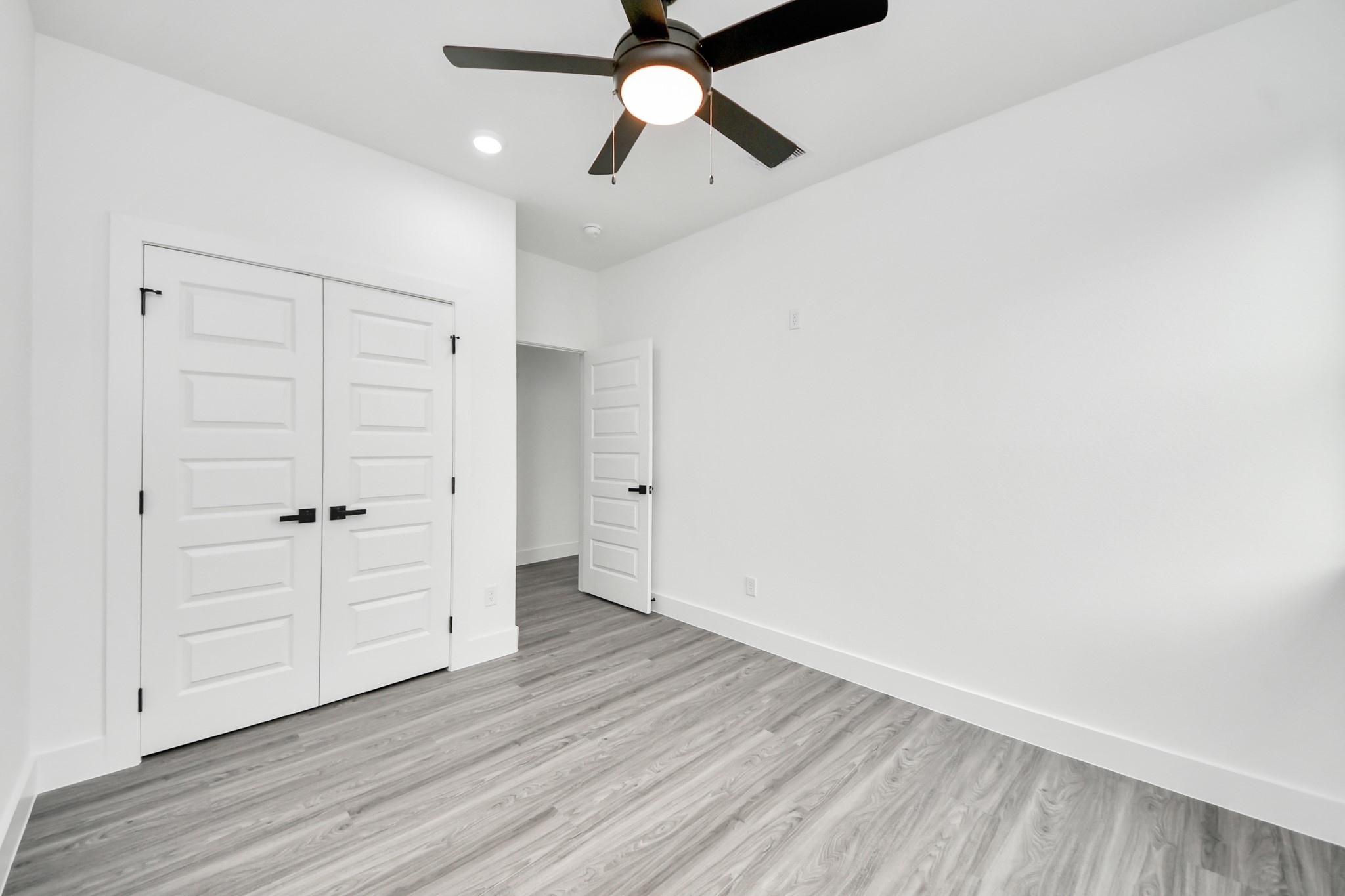 Bright and spacious bedroom featuring sleek laminate flooring, a modern ceiling fan, and ample closet space with stylish white paneled doors.