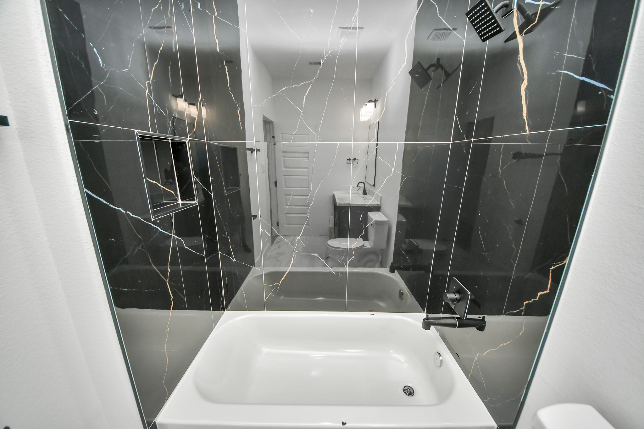 Luxurious bathroom featuring a sleek black marble shower wall with elegant veining, complemented by modern fixtures and a spacious white tub for ultimate relaxation.