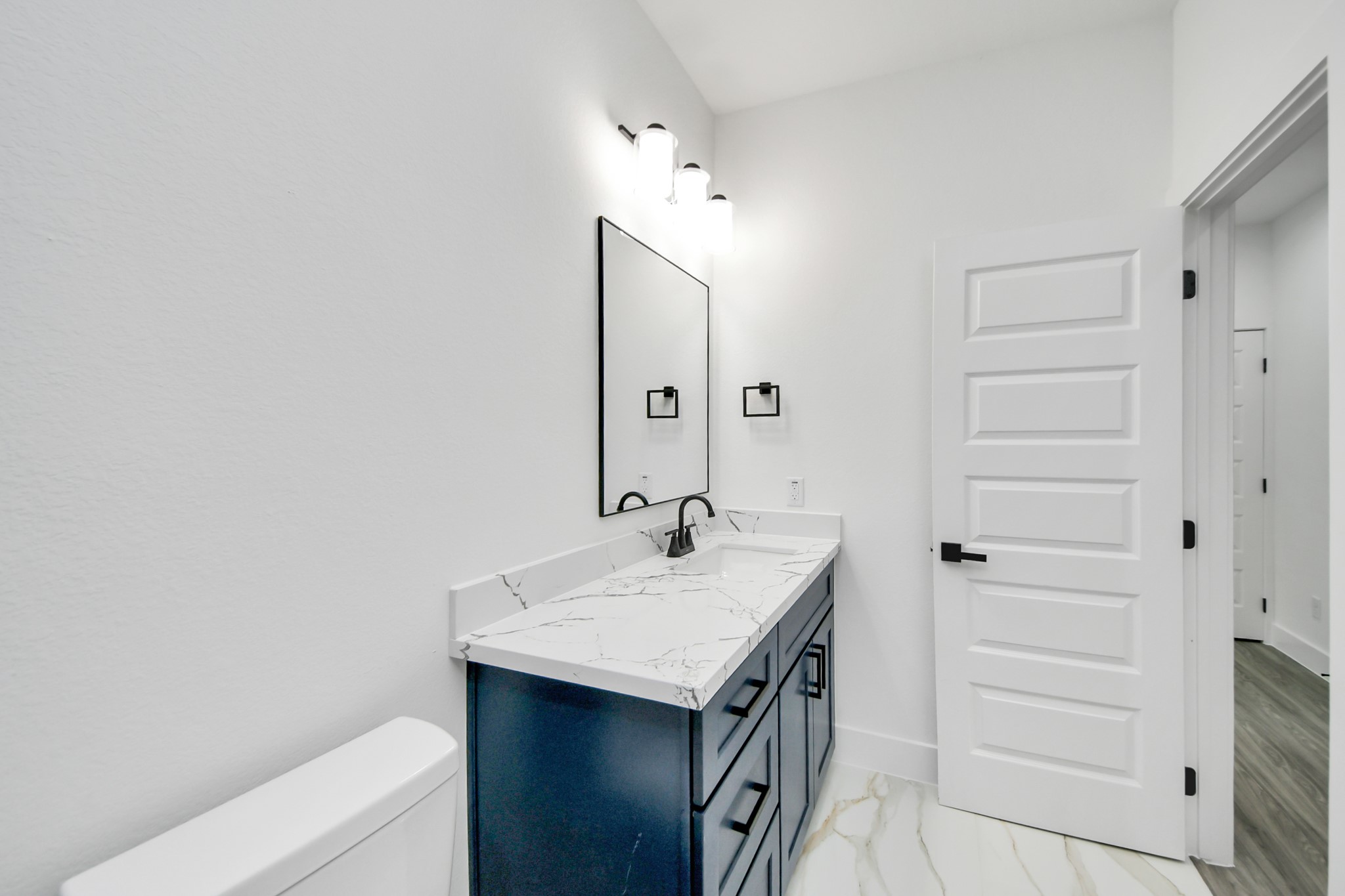 Sleek bathroom featuring a chic navy vanity with elegant marble countertop, complemented by modern fixtures and bright lighting.