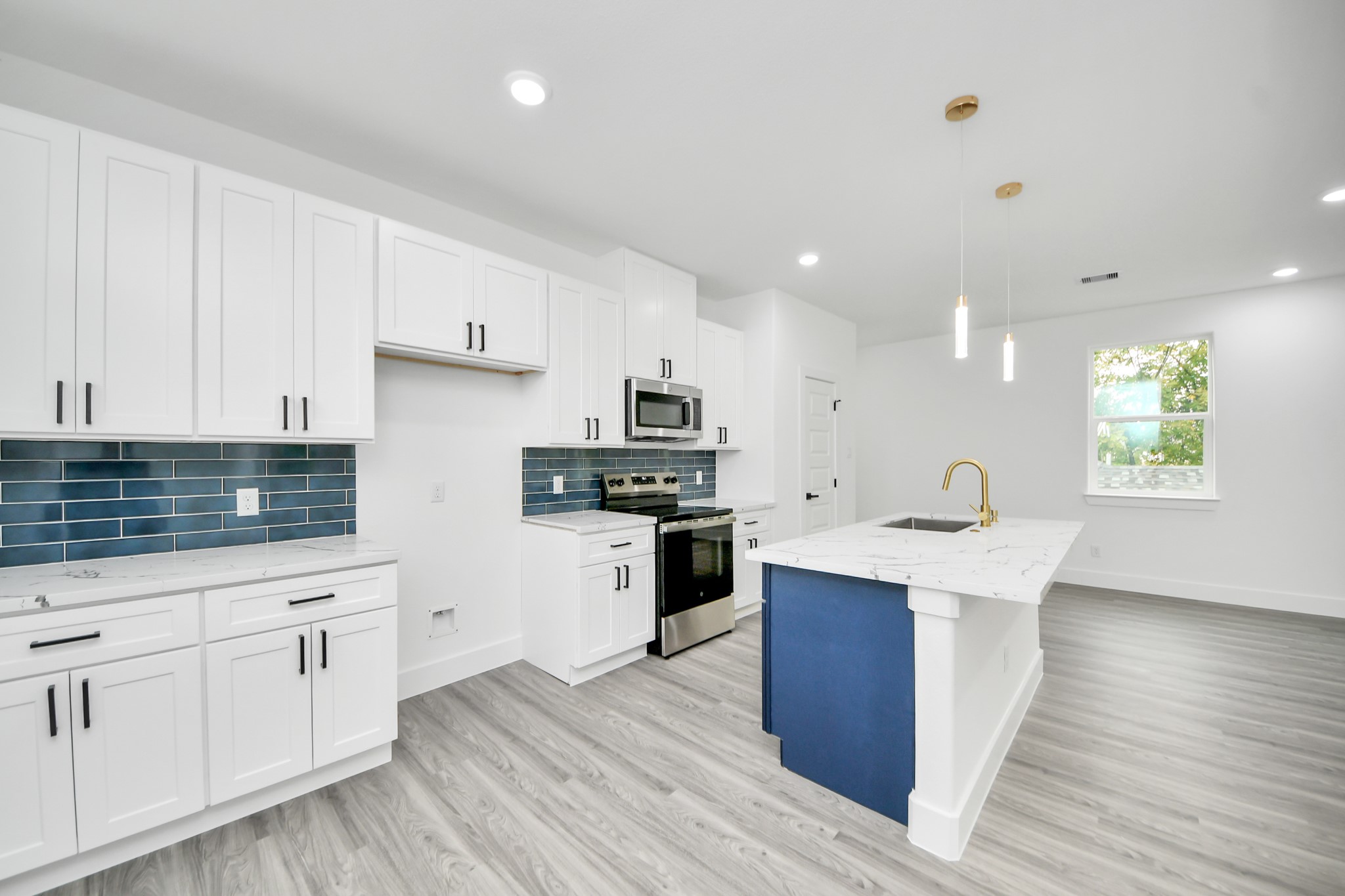 Sleek modern kitchen featuring white cabinetry, stainless steel appliances, and a chic blue tile backsplash. The spacious island with a marble countertop and stylish pendant lighting enhances the contemporary design. Sleek modern kitchen featuring white cabinetry, stainless steel appliances, and a chic blue tile backsplash. The spacious island with a marble countertop and stylish pendant lighting enhances the contemporary design.