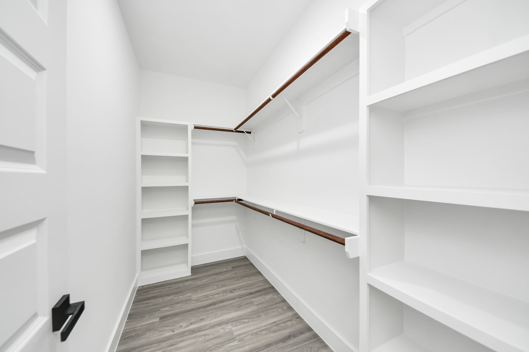 Spacious walk-in closet with ample shelving and hanging space, complemented by sleek wood flooring for a modern touch.