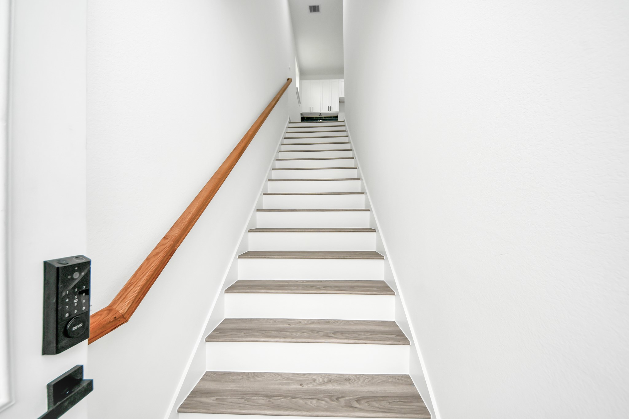 Bright and inviting staircase with modern wood accents leads to the upper level, offering a glimpse of sleek cabinetry at the top.