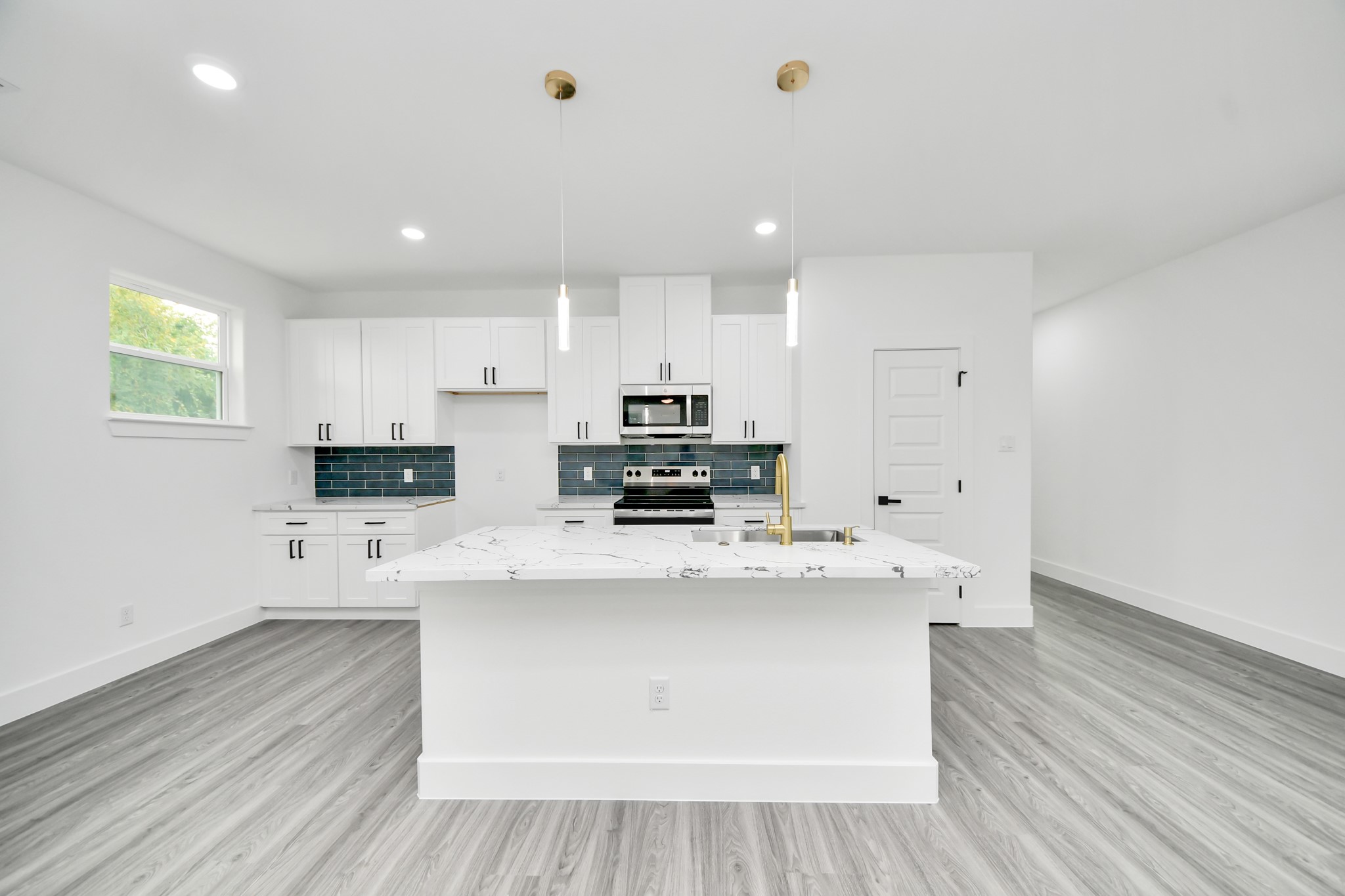 Sleek modern kitchen featuring a spacious island with marble countertops, stainless steel appliances, and elegant pendant lighting. The white cabinetry and stylish blue backsplash add a touch of sophistication.