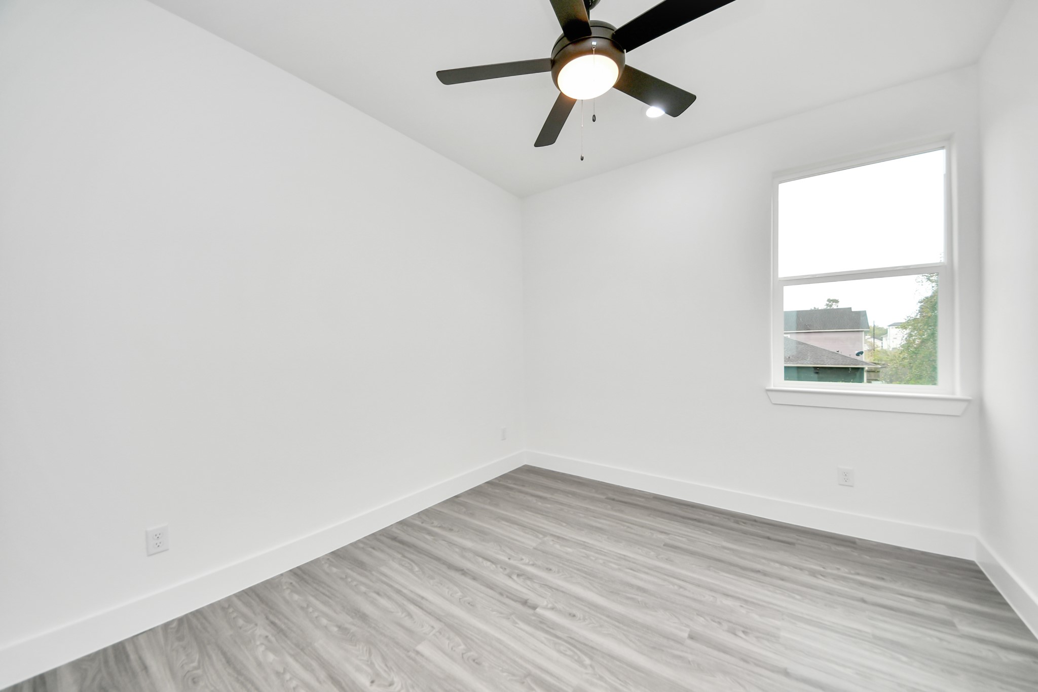Bright and airy bedroom featuring sleek laminate flooring, a modern ceiling fan, and a large window offering plenty of natural light.