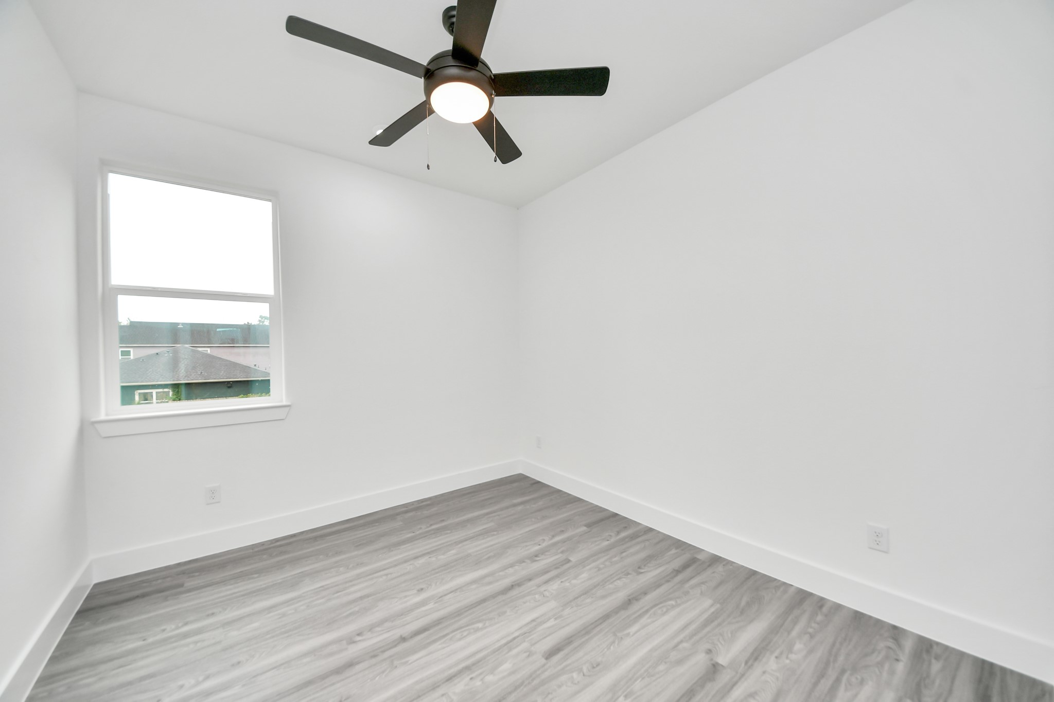 Bright and airy room featuring sleek gray flooring, a modern ceiling fan, and a large window for natural light.