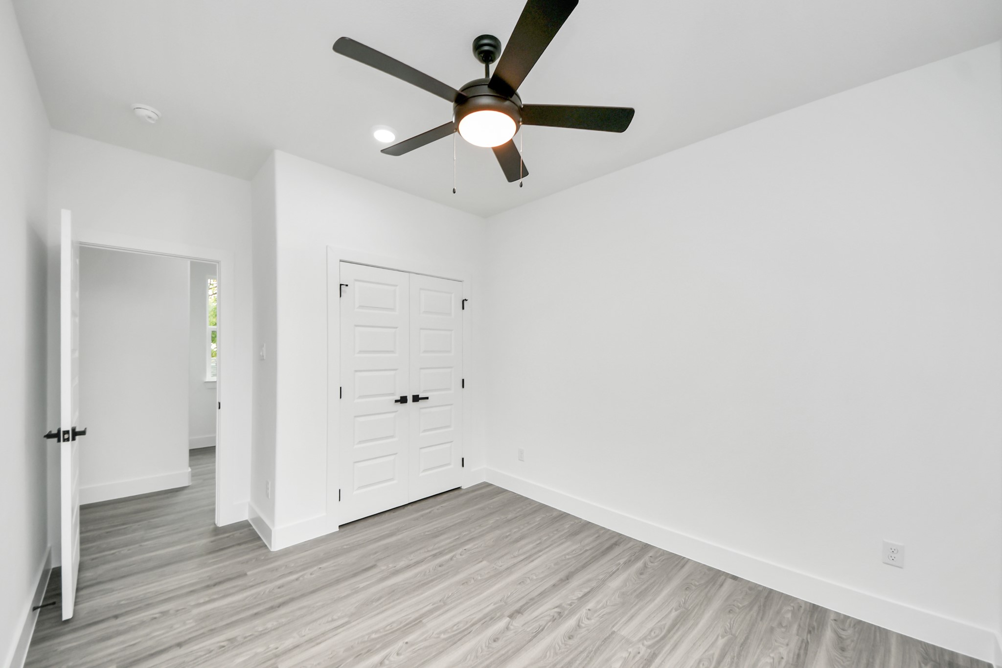Bright and airy room featuring sleek wood flooring, a modern ceiling fan, and ample closet space with double doors.