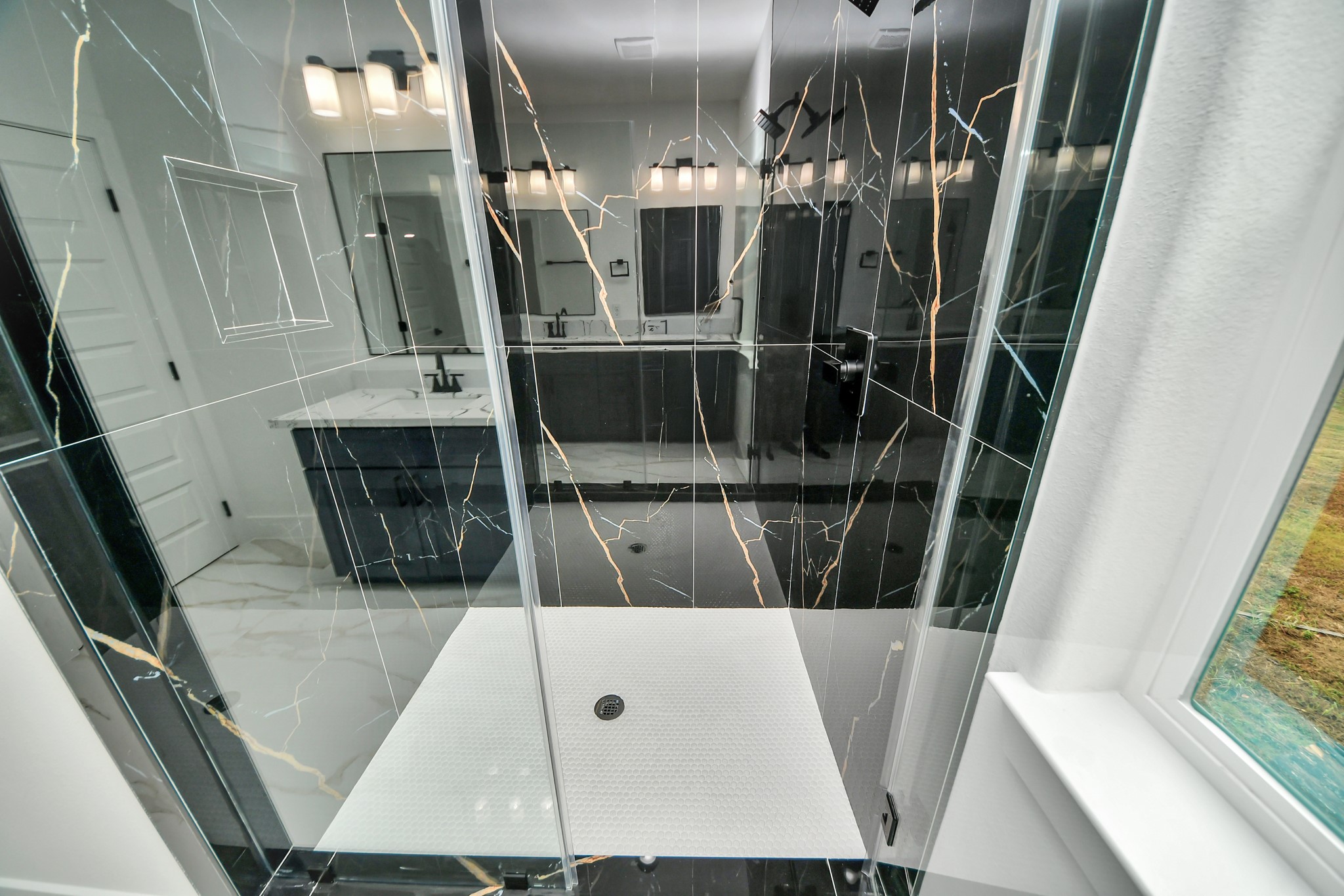 Luxurious bathroom featuring a modern black marble shower with sleek glass doors and elegant fixtures, complemented by a bright vanity area.