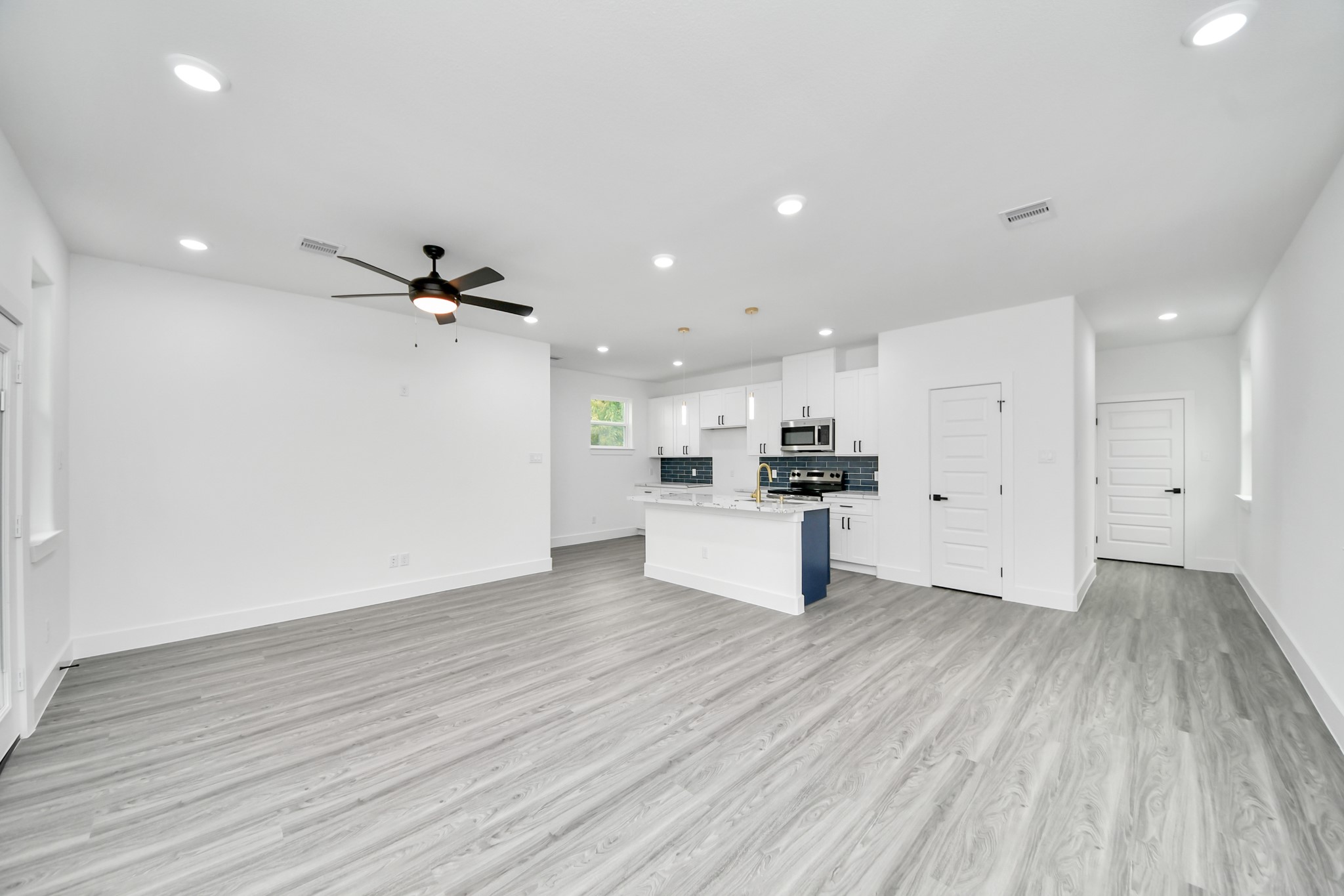 Spacious open-concept living area with modern finishes, featuring sleek laminate flooring, recessed lighting, and a contemporary kitchen with an island and stainless steel appliances.