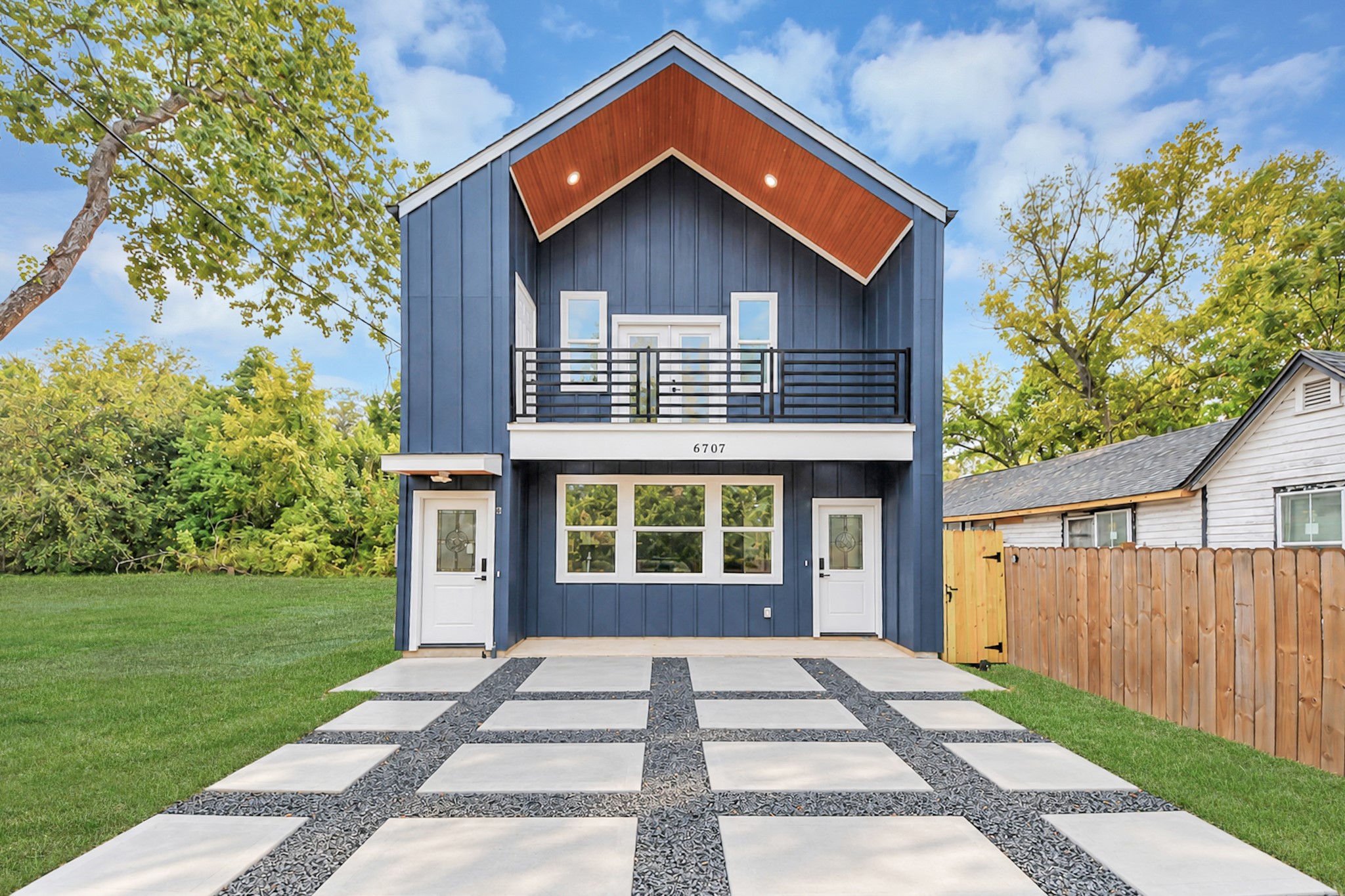 Modern two-story home with a striking blue facade and clean lines, featuring a spacious balcony and a unique checkered driveway. Modern two-story home with a striking blue facade and clean lines, featuring a spacious balcony and a unique checkered driveway.