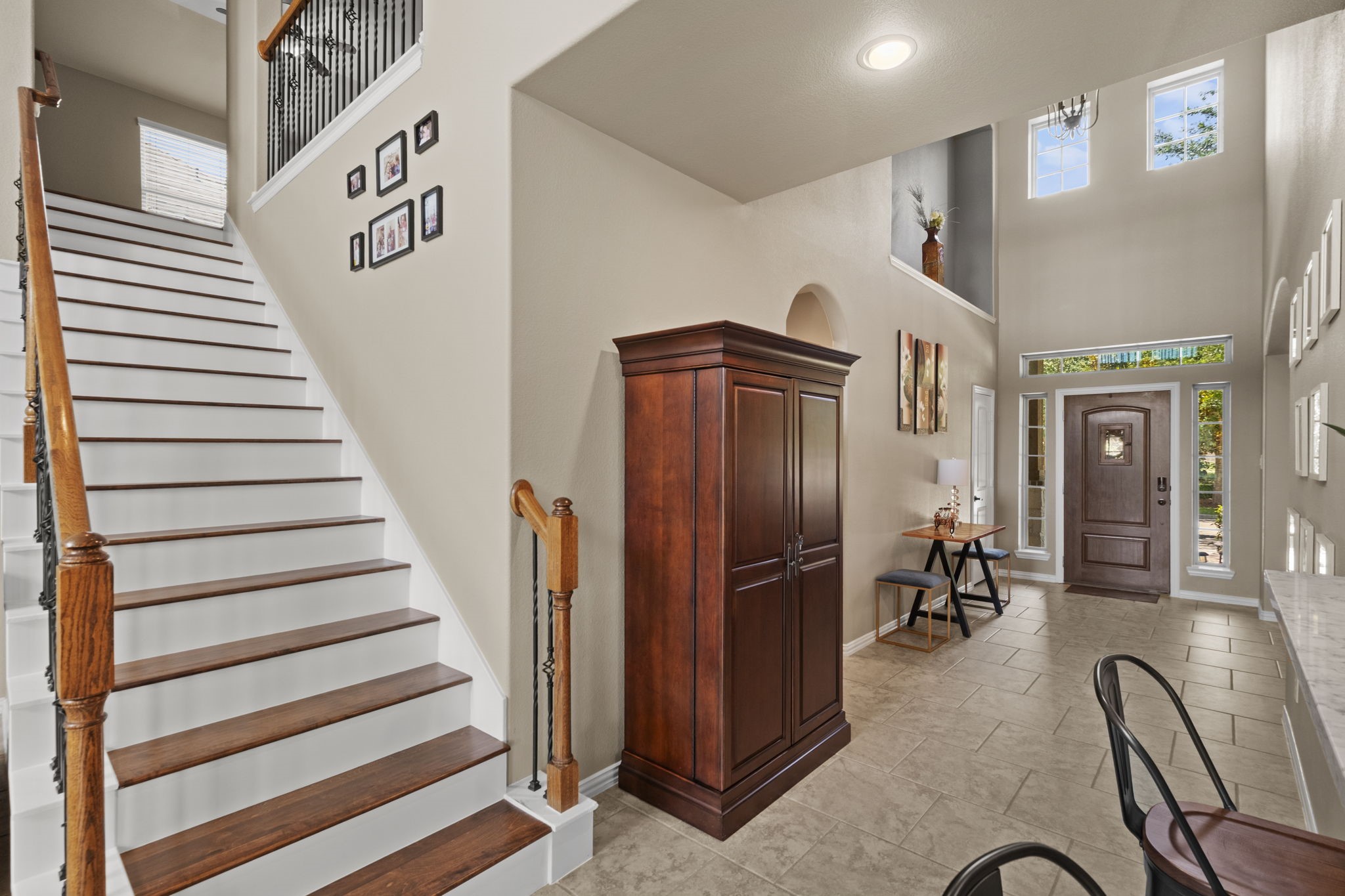 This welcoming entryway features high ceilings and abundant natural light. The space includes a wooden staircase with iron accents.The front door is flanked by sidelights, enhancing the airy feel of the foyer.