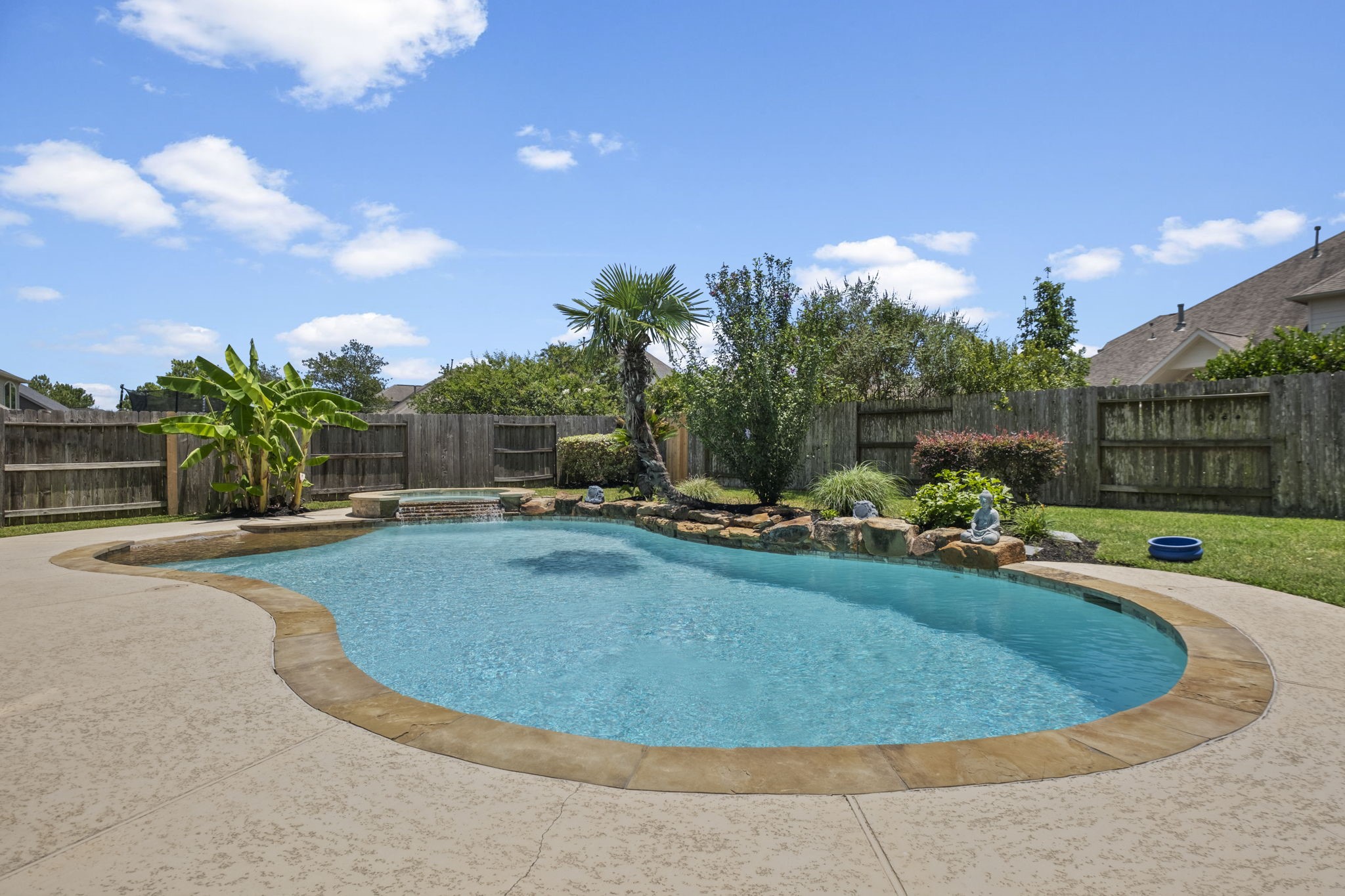 This backyard features a beautifully landscaped pool with a rock waterfall, surrounded by lush greenery and a privacy fence, creating a private oasis perfect for relaxation.