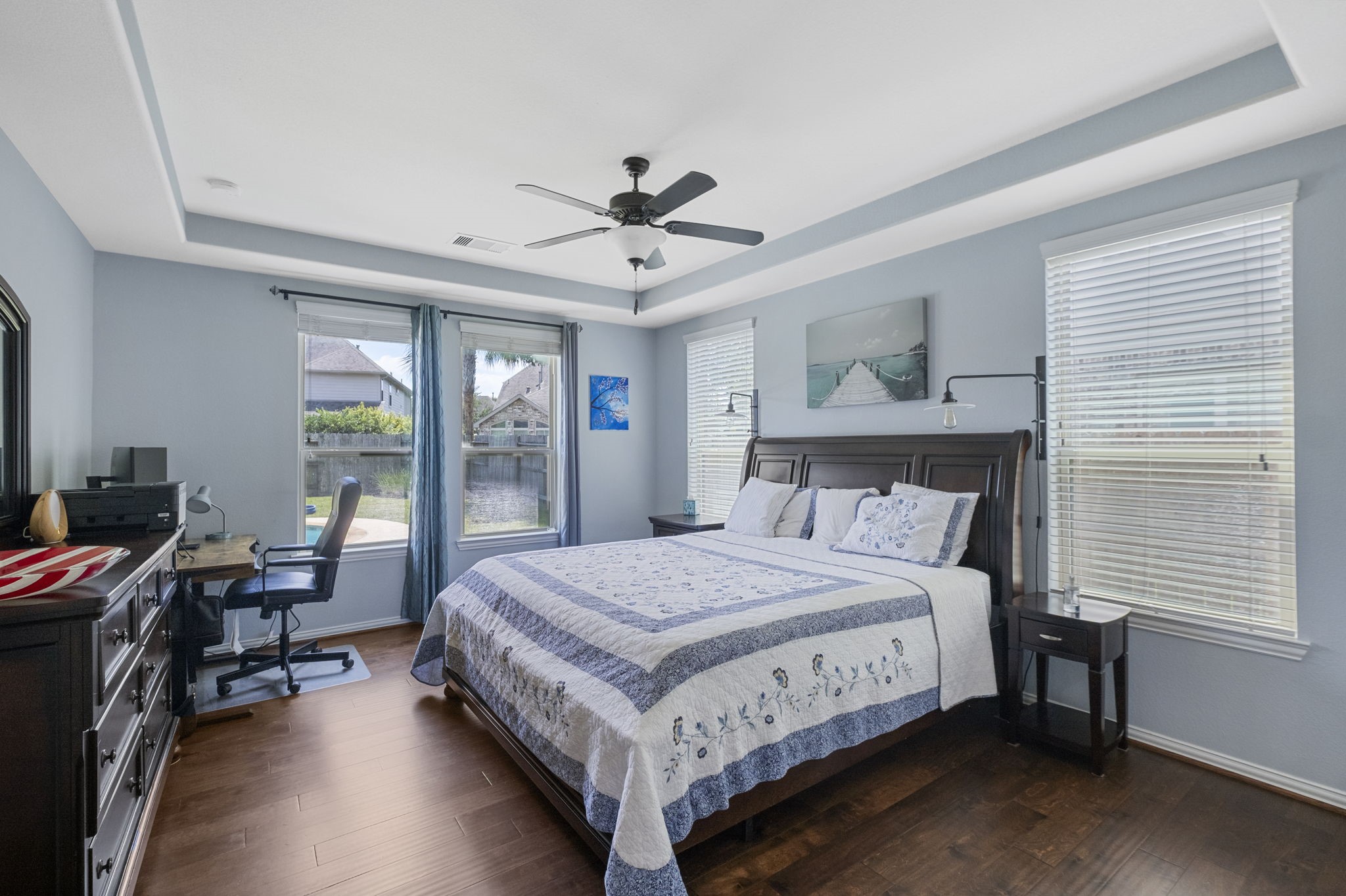 Primary bedroom with wood flooring & tray ceilings offers wonderful backyard views.