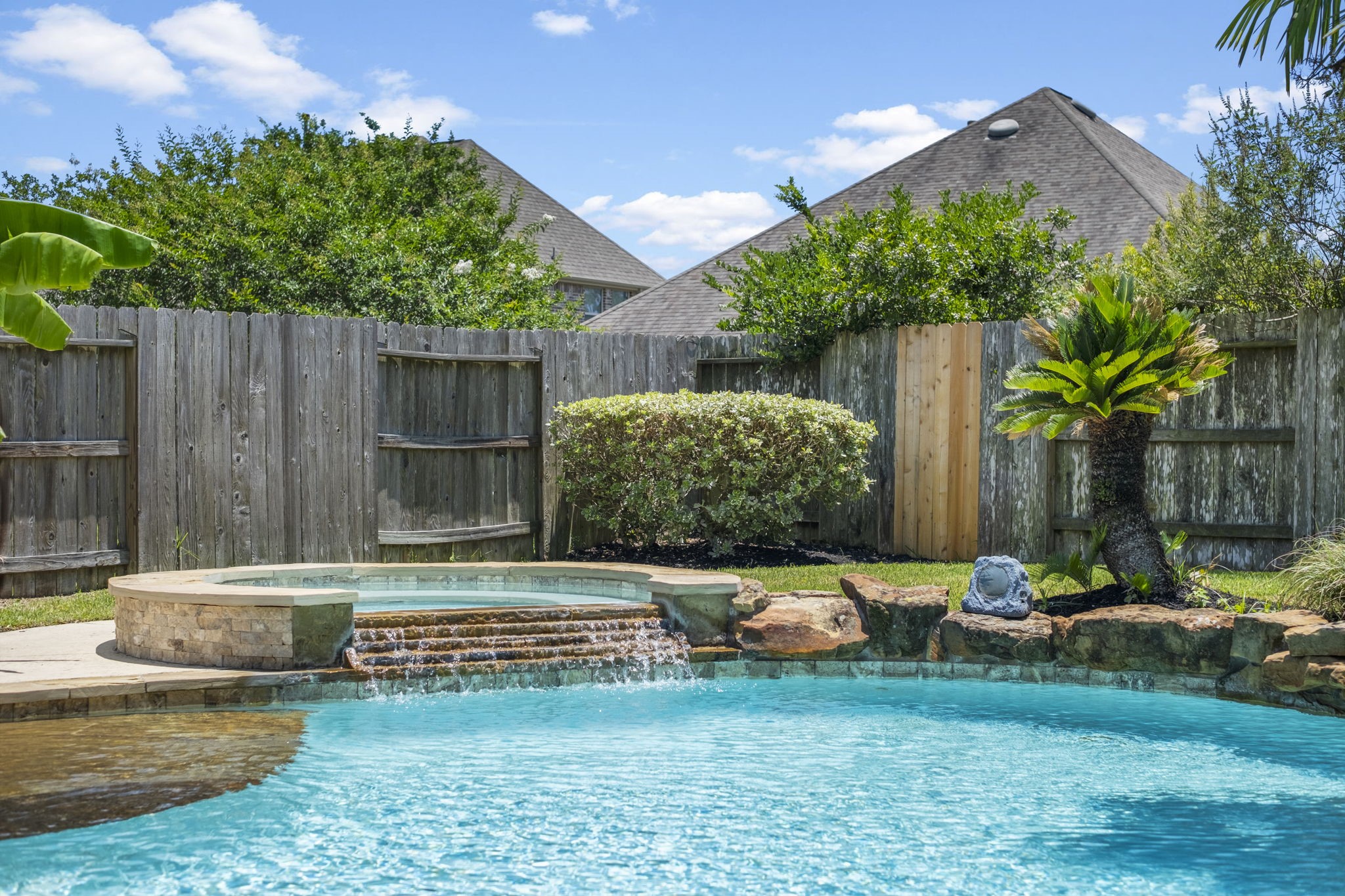 This backyard oasis features a sparkling pool with a connected hot tub, framed by lush greenery, perfect for relaxation and entertaining.