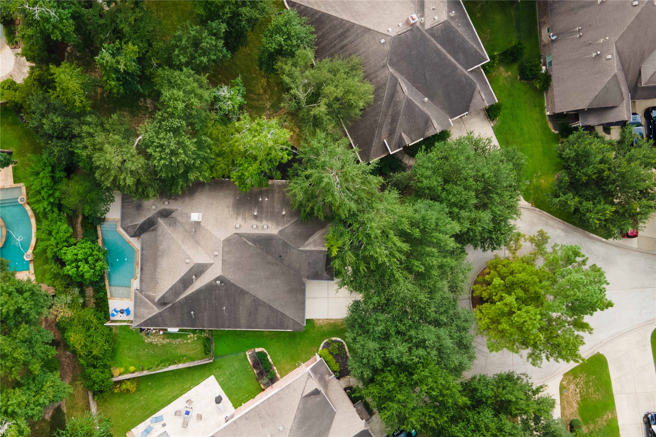 This aerial view shows the home in the center surrounded by lawn space and mature trees, the private pool, and the cul-de-sac on the right.