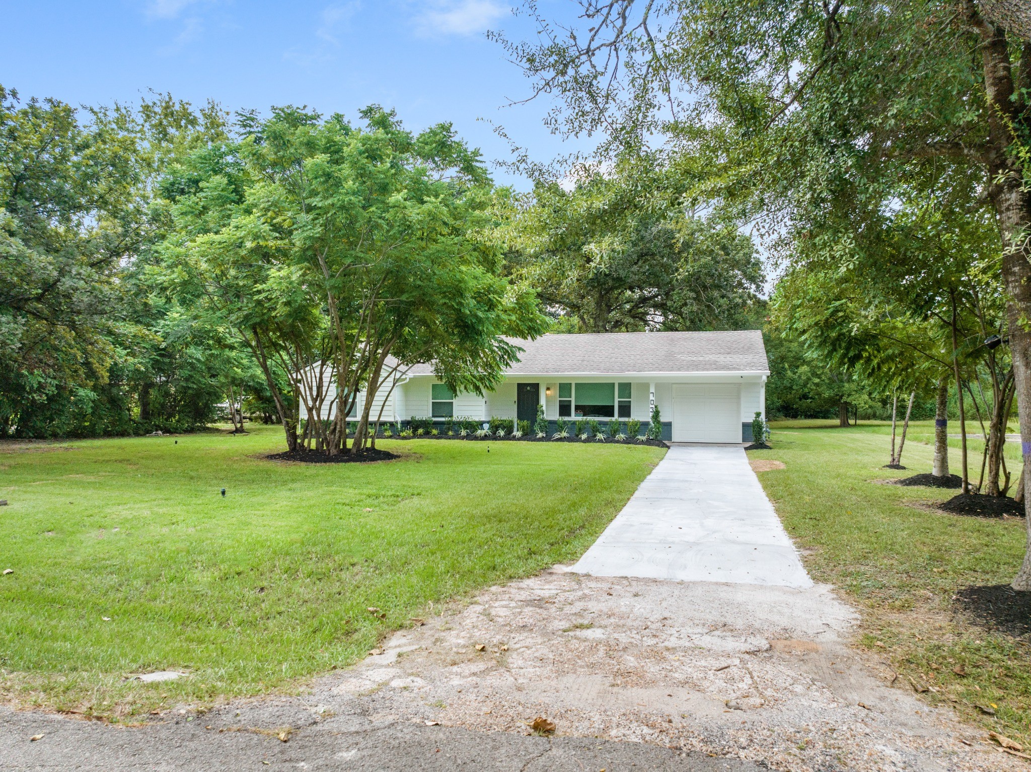 Long driveway leads through the tree-lined front lawn to the home, showcasing the depth and scale of the nearly one-acre property.